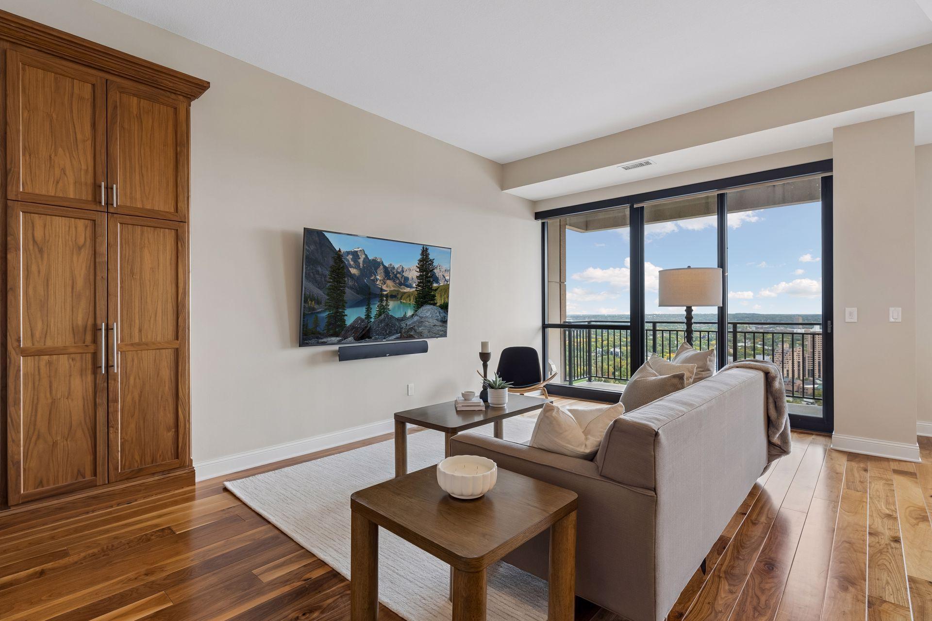 Condo living room with wood cabinetry, a gray sofa, and floor-to-ceiling windows overlooking the city.