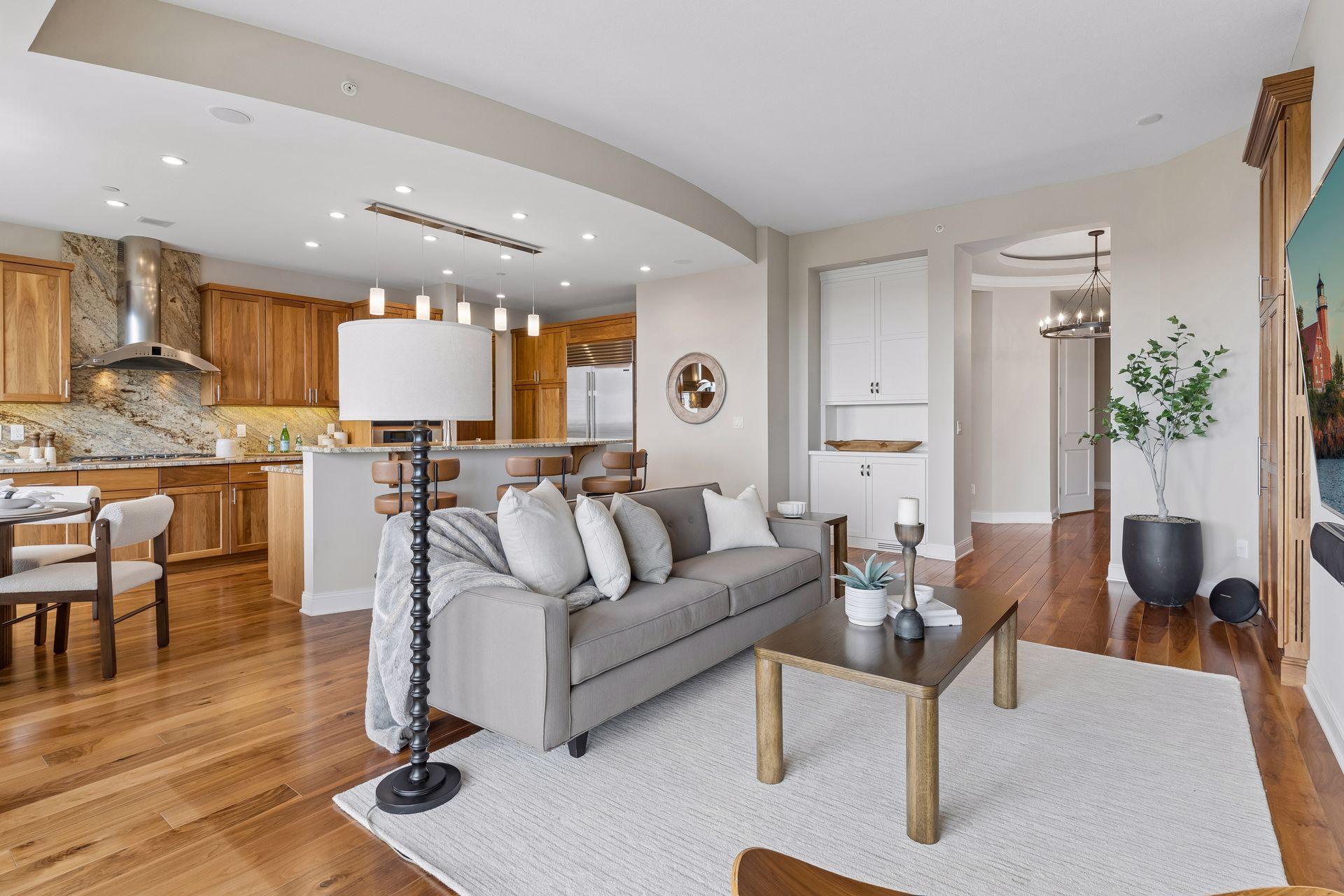 Open-plan kitchen and living room with warm wood cabinets, granite counters, hardwood floors, and a gray sofa.