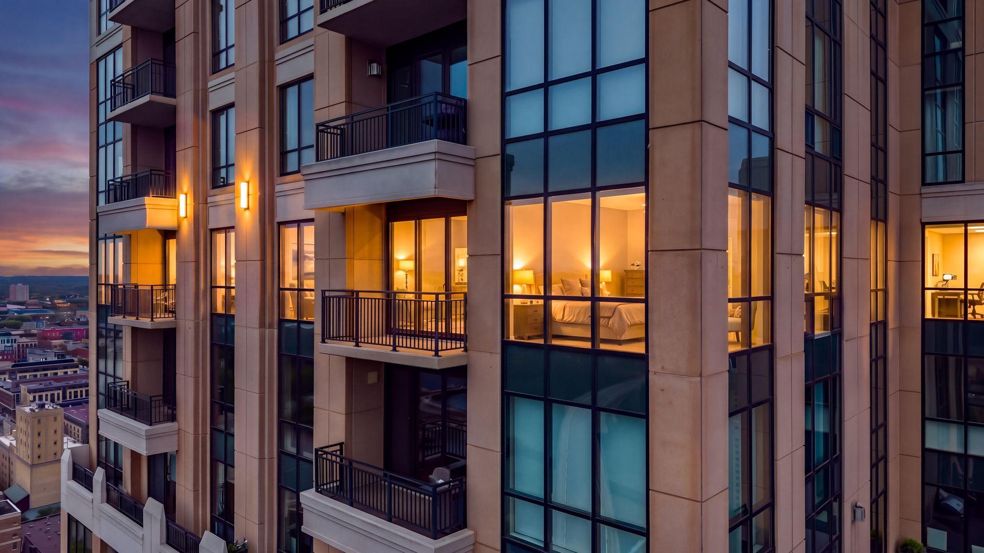 High-rise condominium exterior at dusk, with balconies and warmly lit interiors overlooking the city.