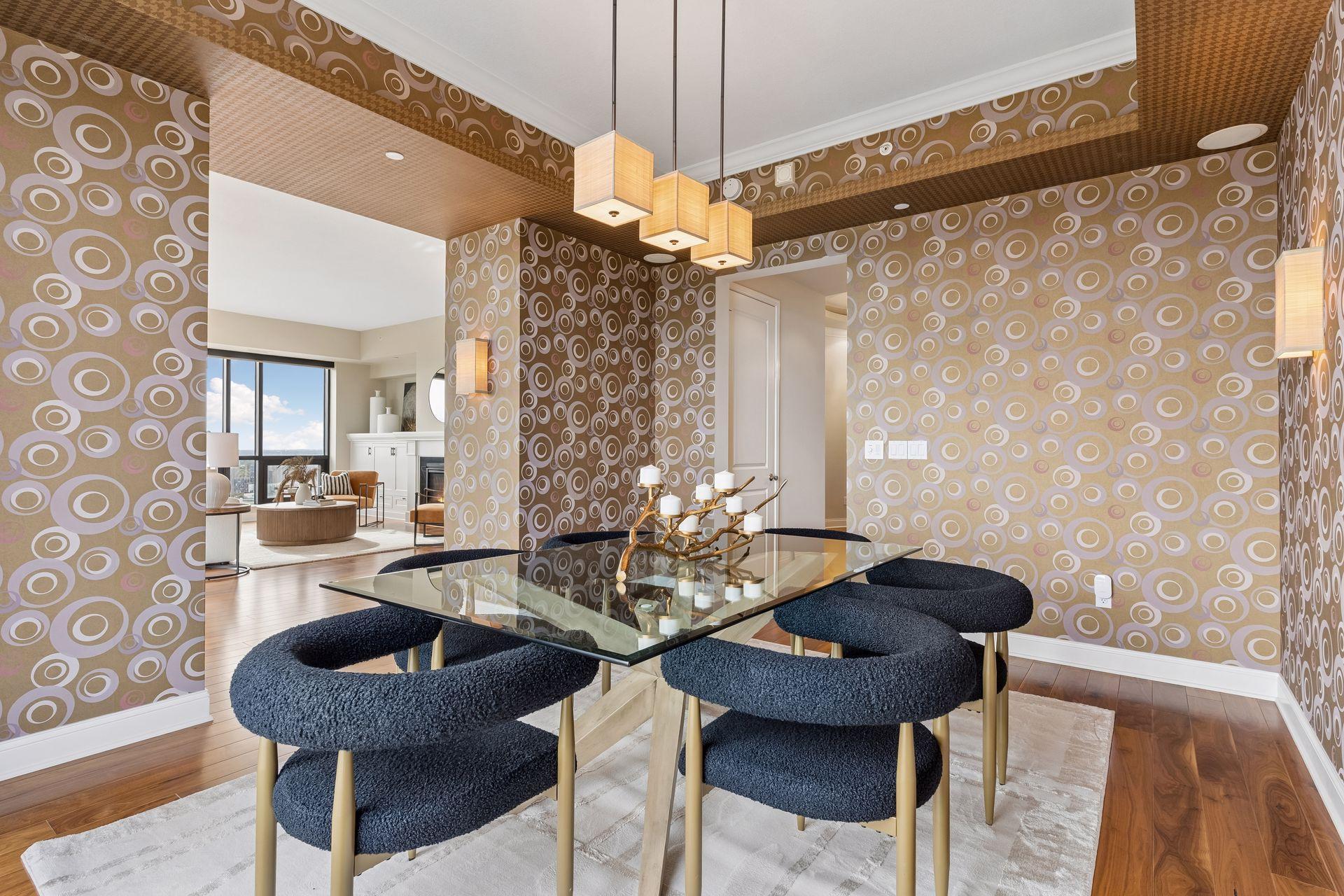 Dining area with circular-patterned wallpaper, a glass table, navy chairs, and square pendant lights.