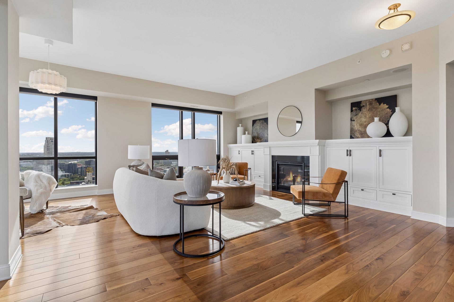 Furnished condo living room with a fireplace, hardwood floors, and expansive city-view windows.