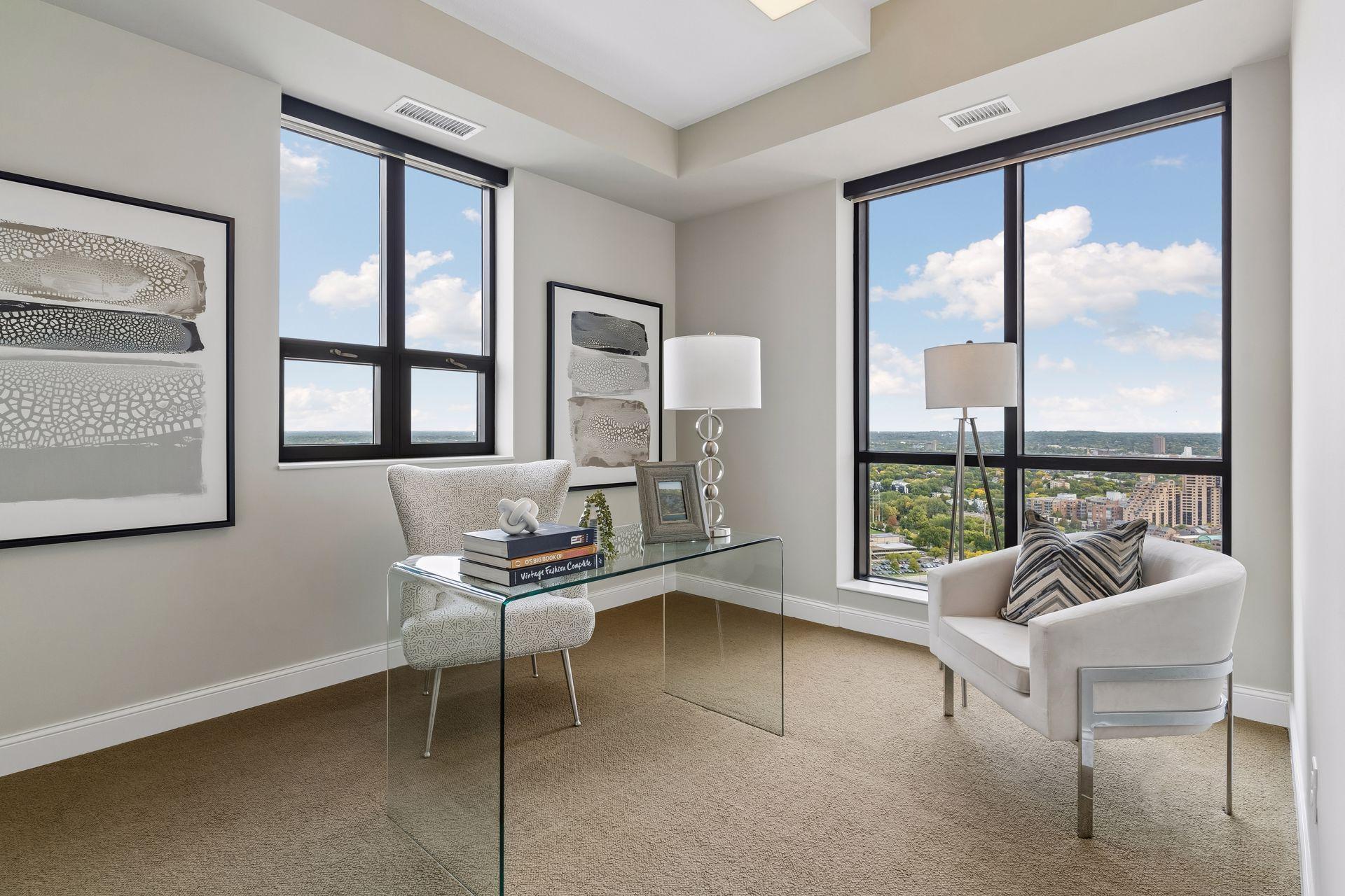 Furnished condo study with a glass desk and city views through large windows.