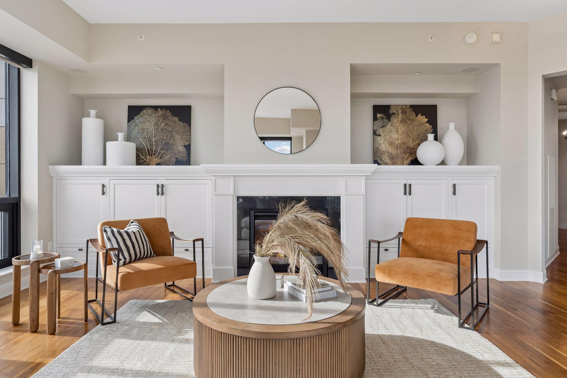Staged living room with a white built-in fireplace, rust-colored armchairs, and a round coffee table.