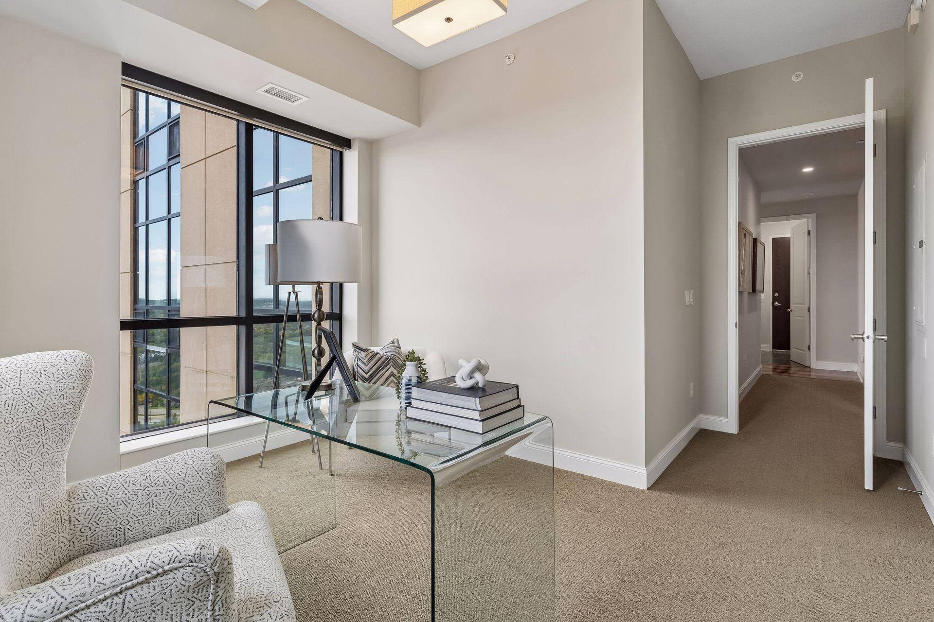 Staged condo living room with floor-to-ceiling windows, a glass coffee table, and an open hallway.