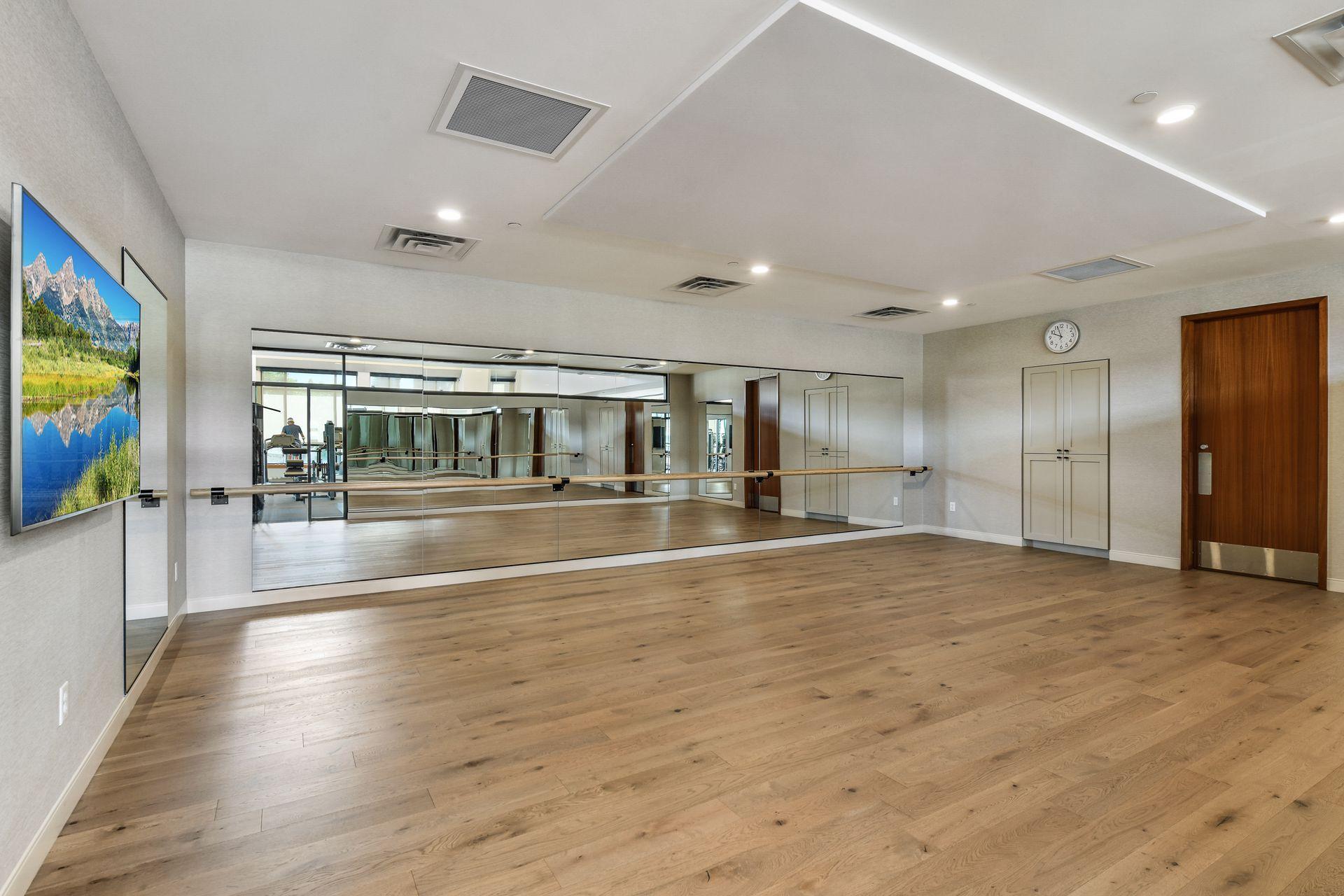 Fitness studio with mirrored walls, a wooden ballet barre, and light wood flooring.