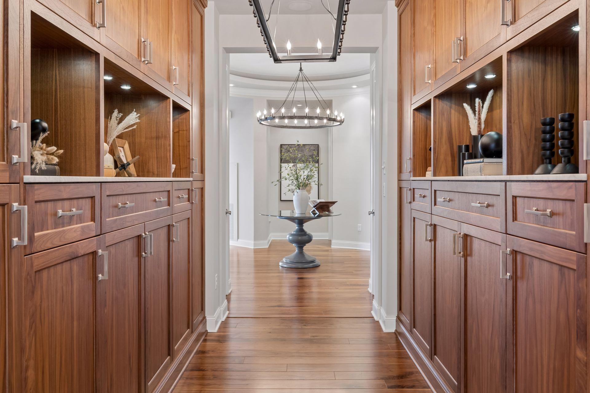 Walnut-paneled hallway with illuminated display shelves opening to a chandelier-lit room.