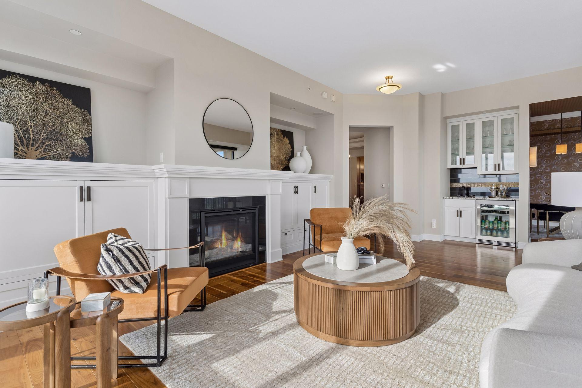 Staged condo living room with a built-in fireplace, tan leather chairs, and round wood coffee table.