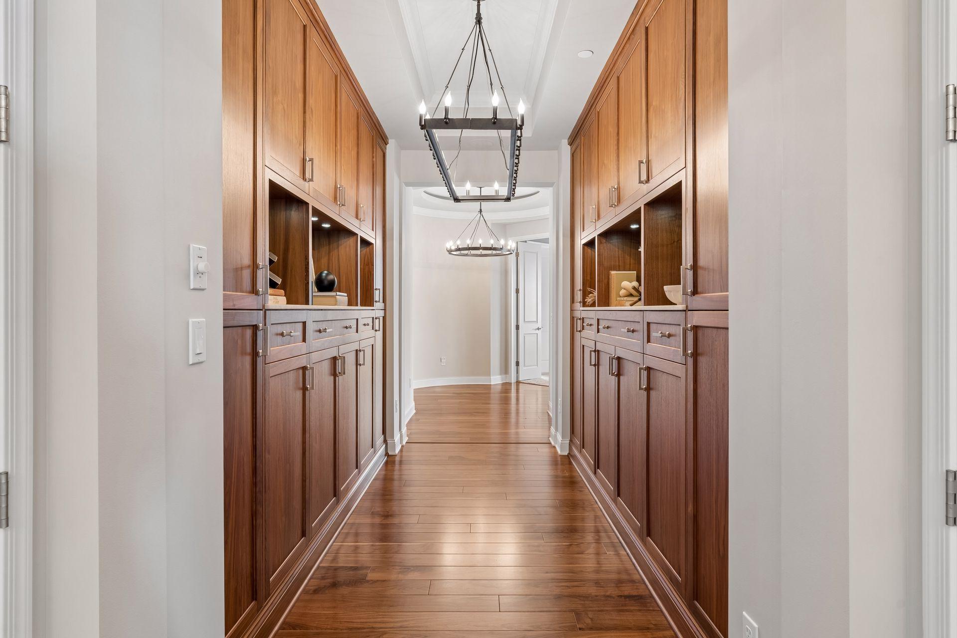 Hallway with dark wood built-in cabinetry, hardwood floors, and two chandeliers.