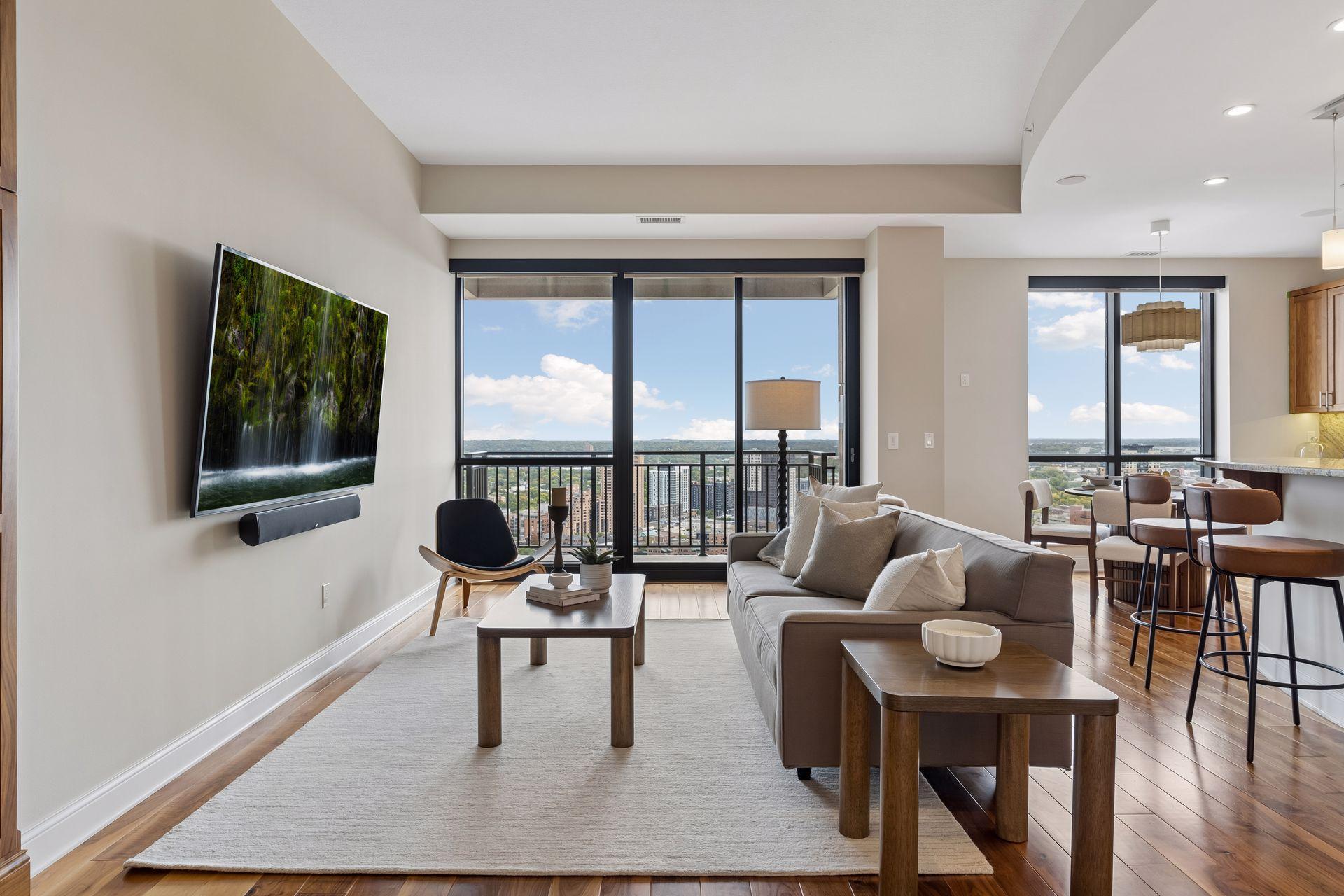 Furnished condo living room with floor-to-ceiling windows overlooking the city.