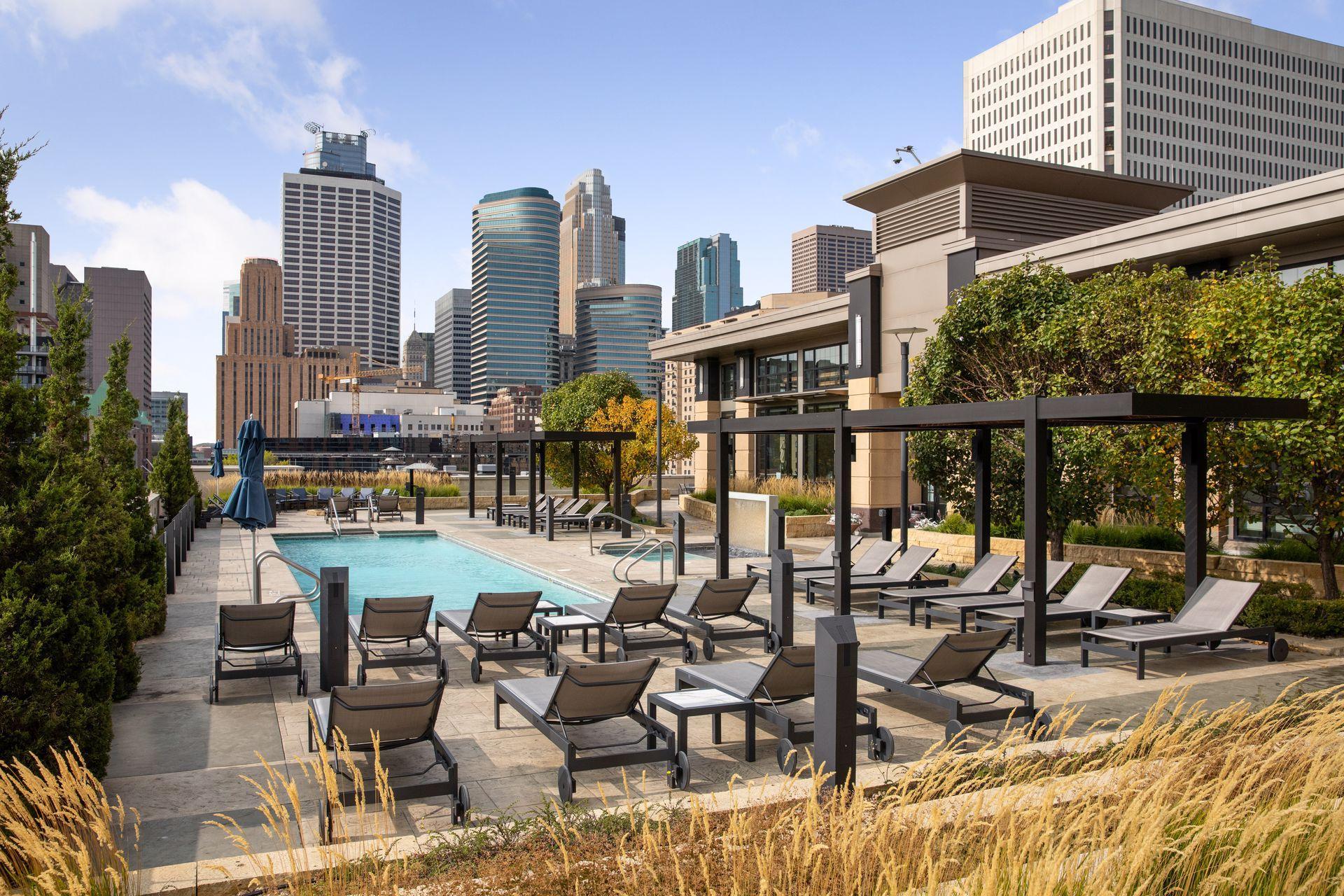 Rooftop pool deck with lounge chairs and pergolas overlooking the Minneapolis skyline.