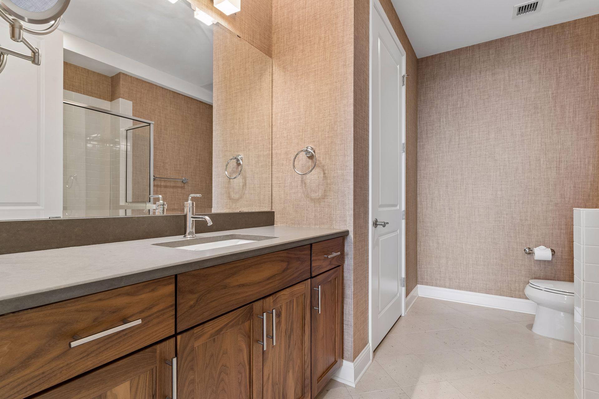 Bathroom with a long wood vanity, large mirror, glass shower and toilet.