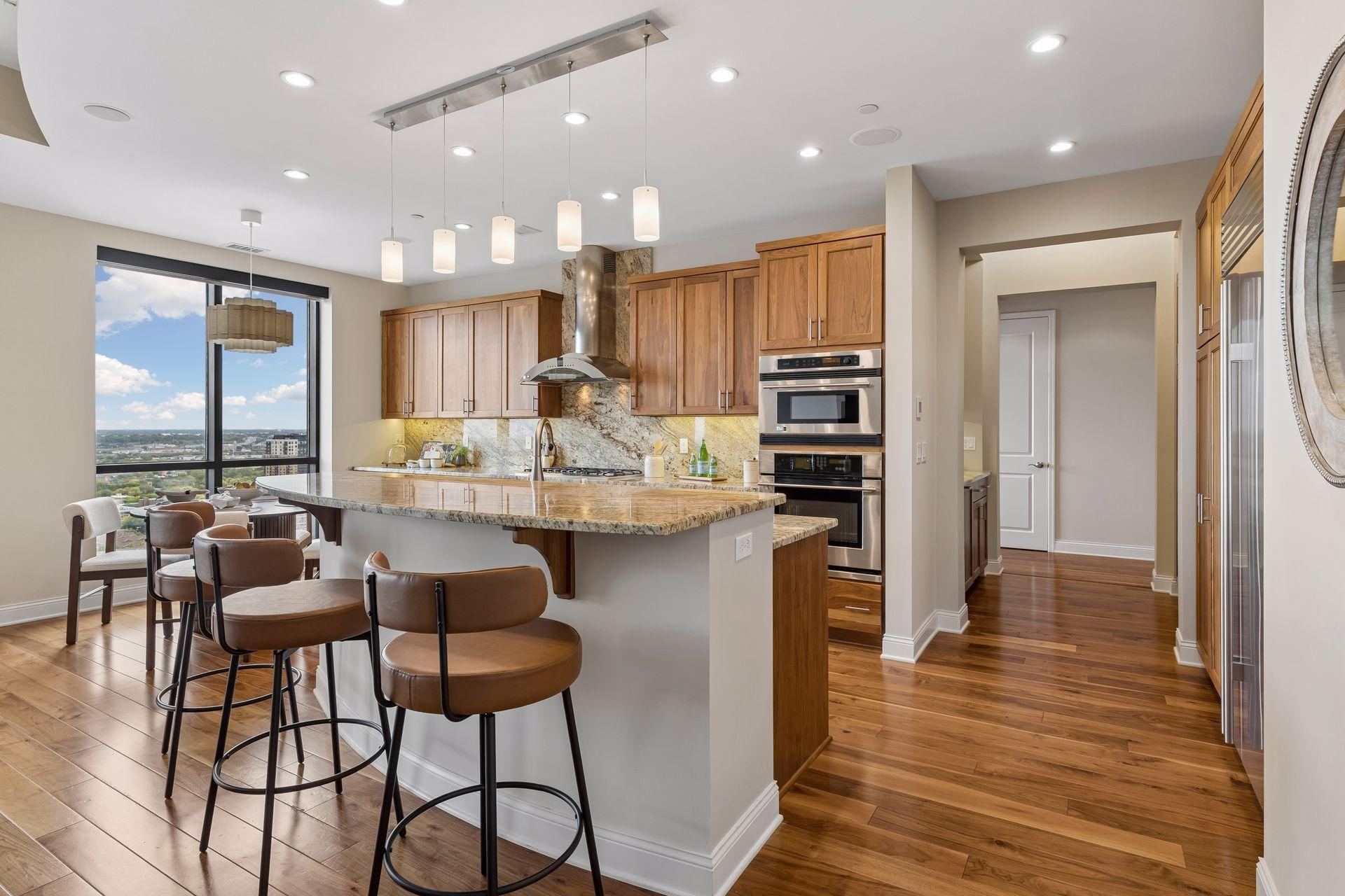 Condo kitchen with wood cabinetry, a granite island, and city views through large windows.