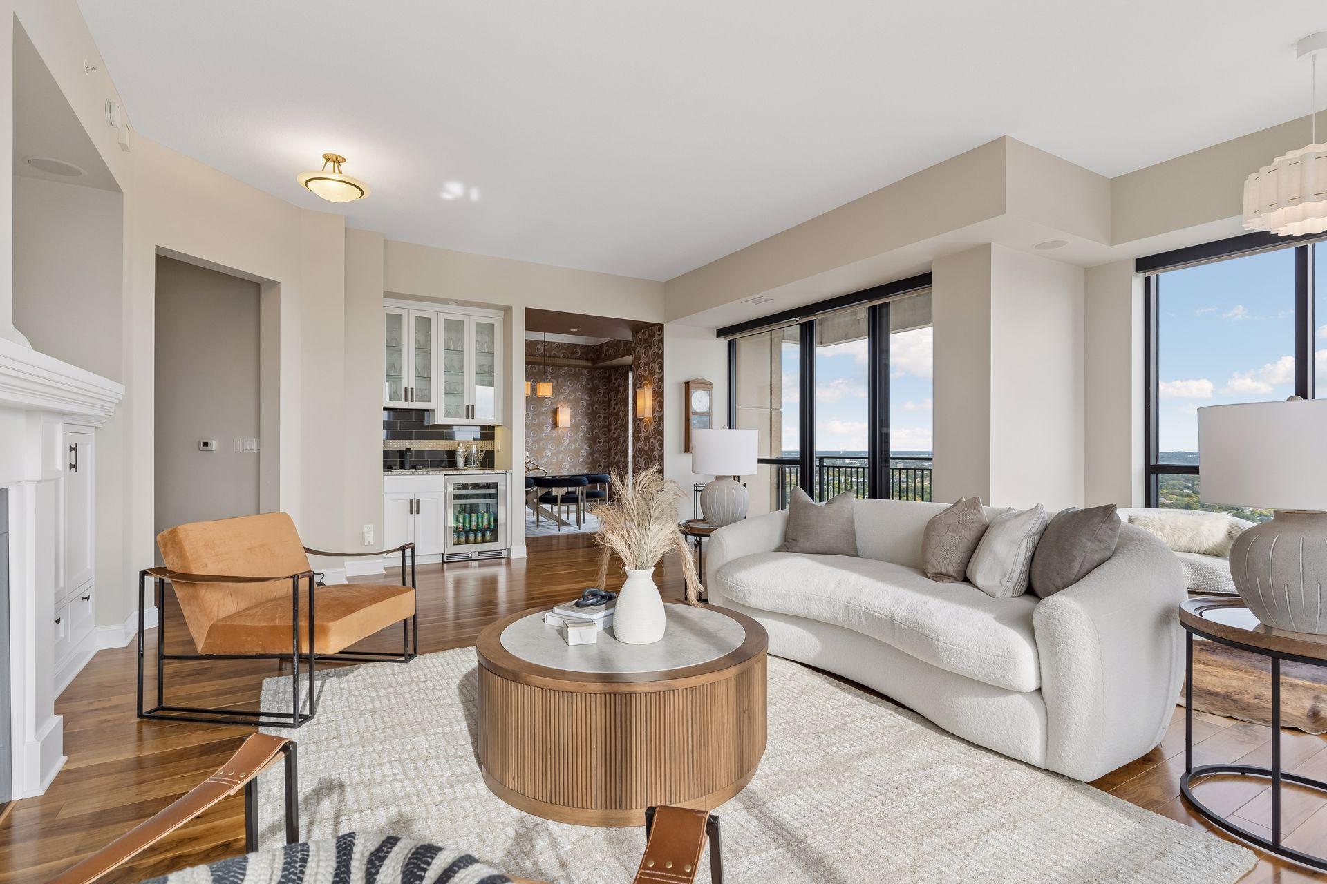 Living room with a white sofa, wood coffee table, fireplace, and large windows overlooking greenery.