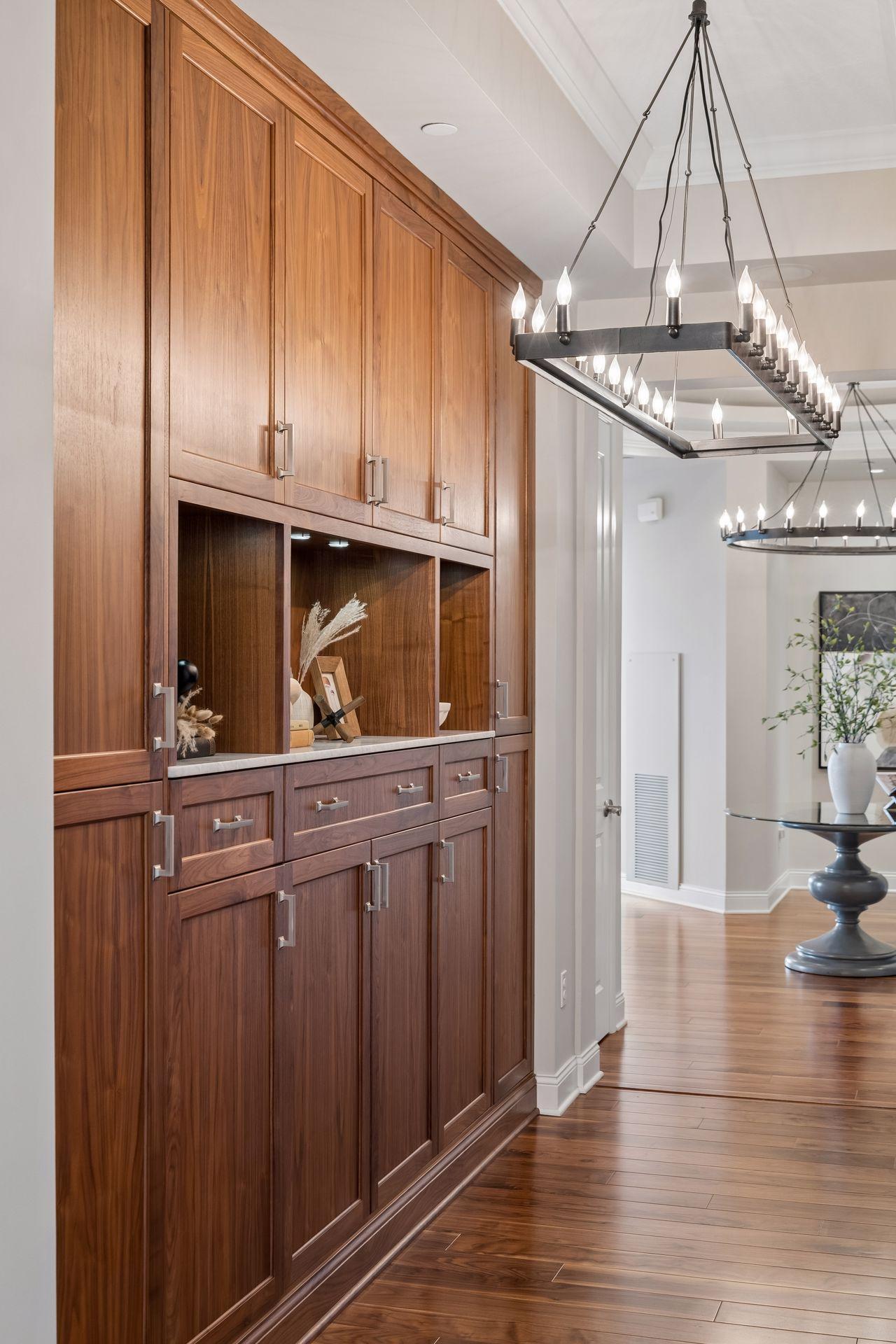 Walnut built-in cabinetry and display shelves beneath modern chandeliers in a bright condo interior.