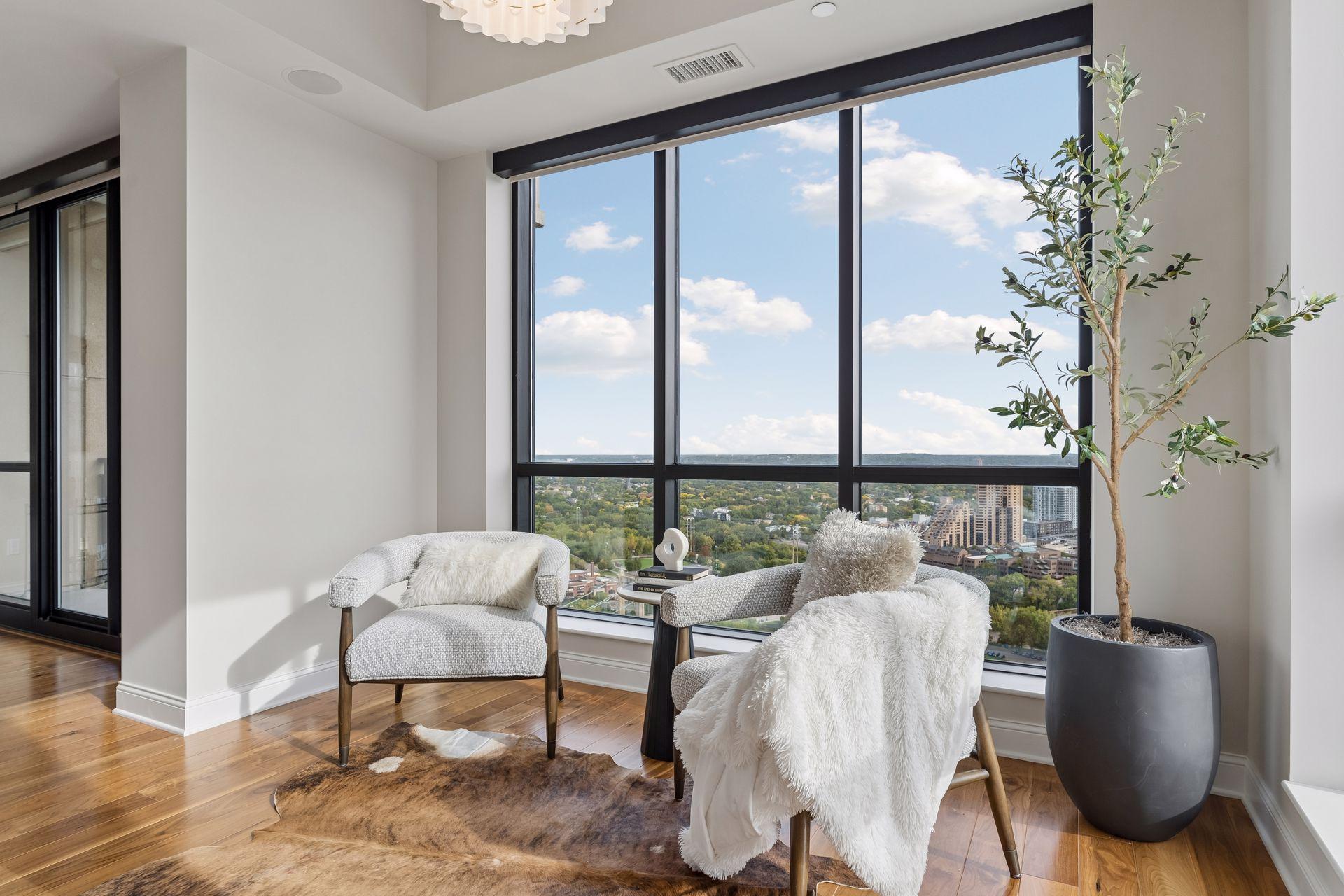 Condo sitting area with two chairs by floor-to-ceiling windows overlooking greenery and distant water.