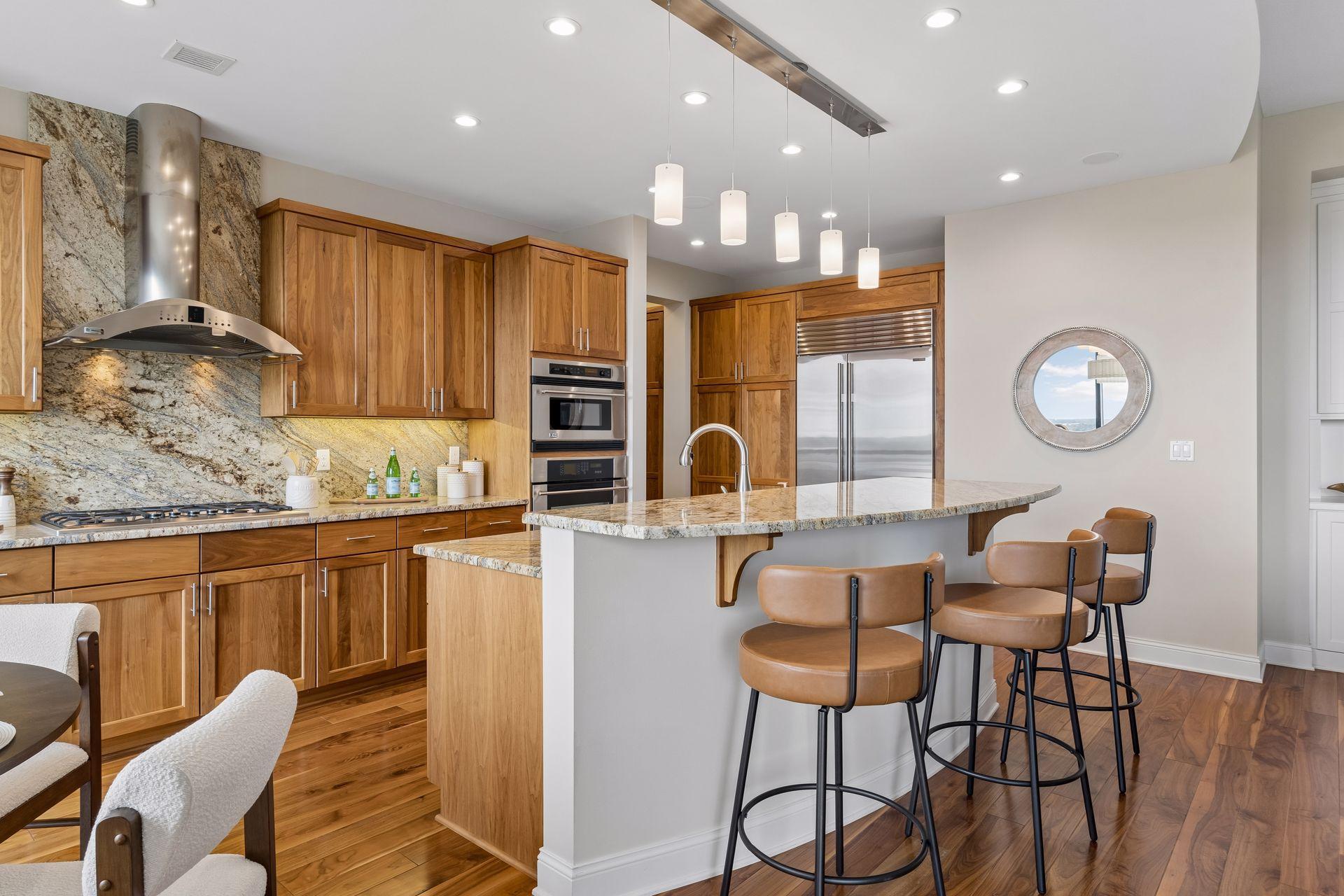 Modern kitchen with warm wood cabinetry, a stone backsplash, and a large island with leather bar stools.