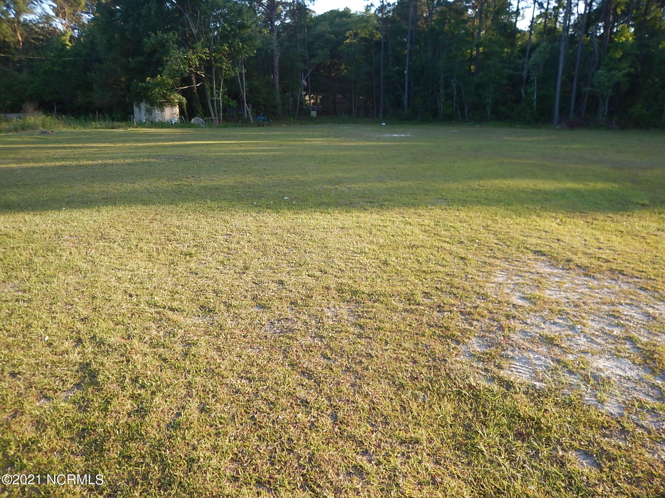 Grassy vacant lot with an open clearing and woods along the rear boundary.