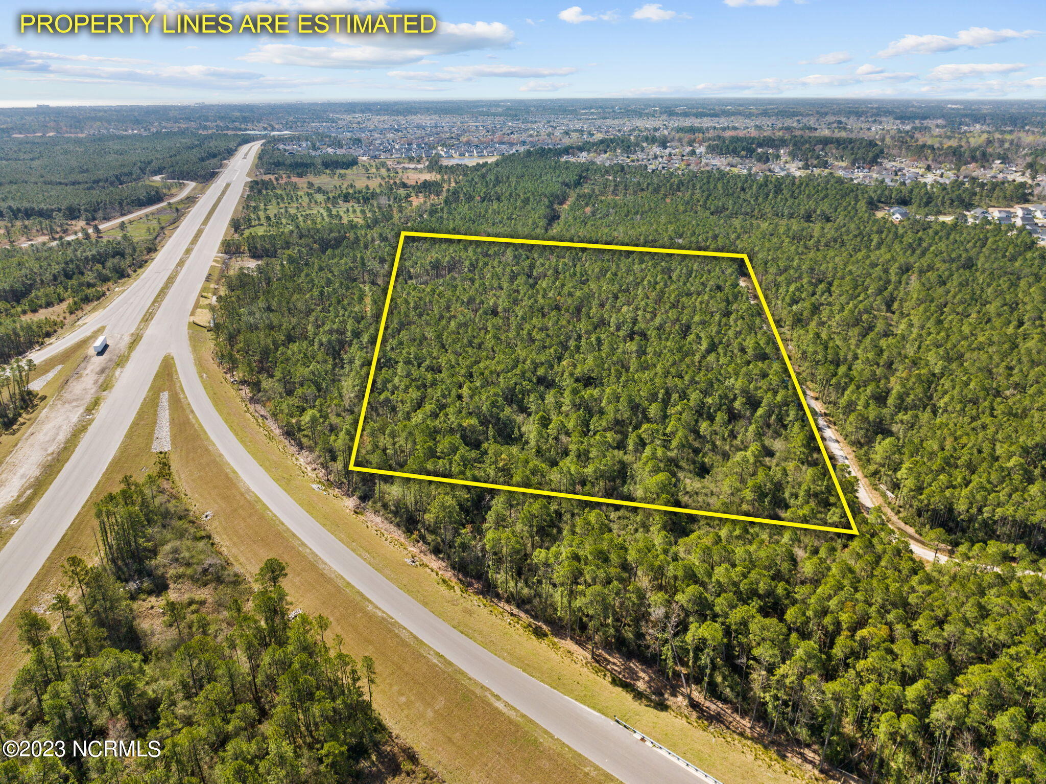 Aerial view of a wooded parcel outlined in yellow beside a curving road.