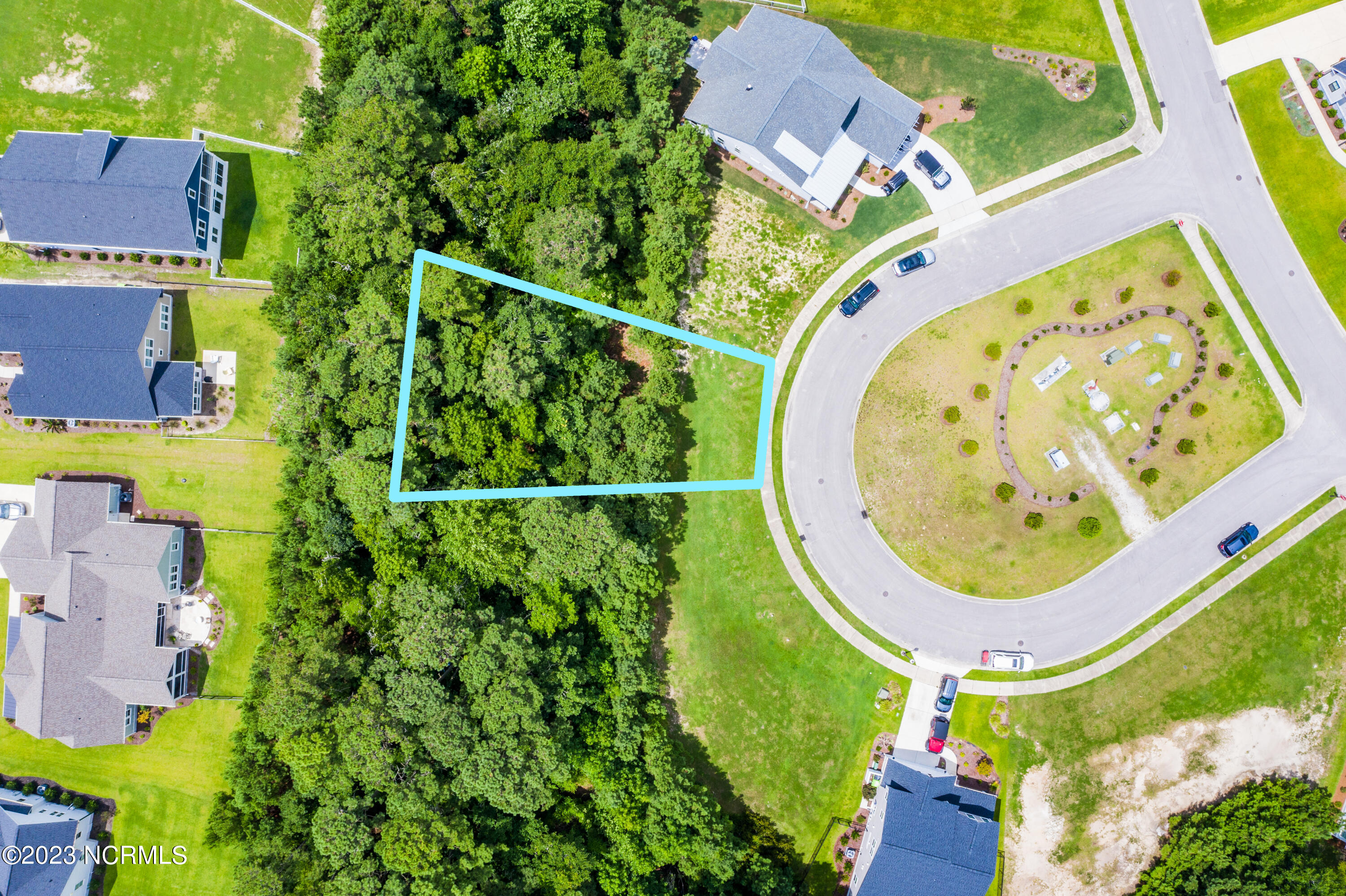 Aerial view of a wooded lot outlined in turquoise beside a curved neighborhood street.