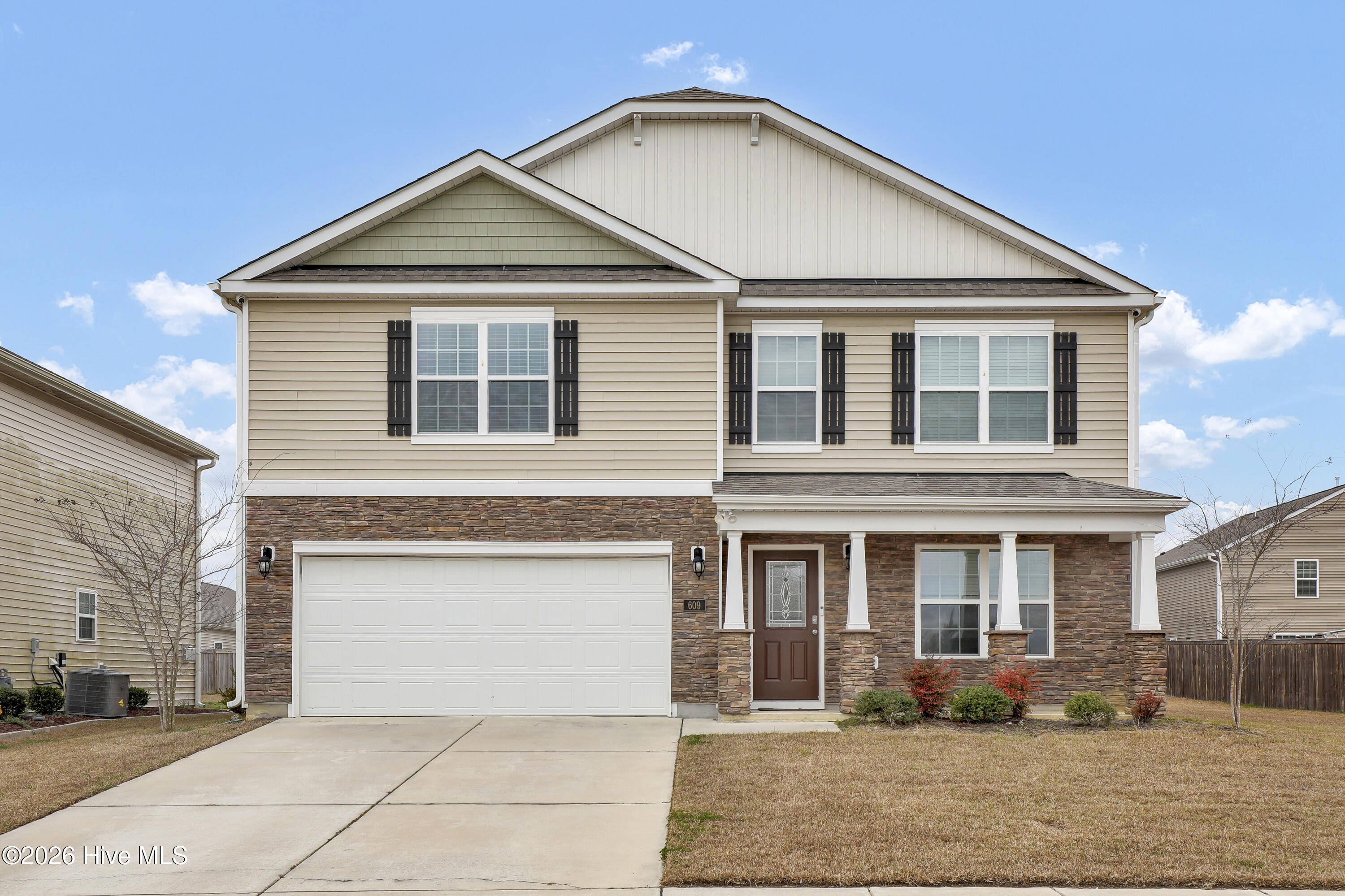 Two-story beige house with stone accents, a two-car garage, and a covered front porch.