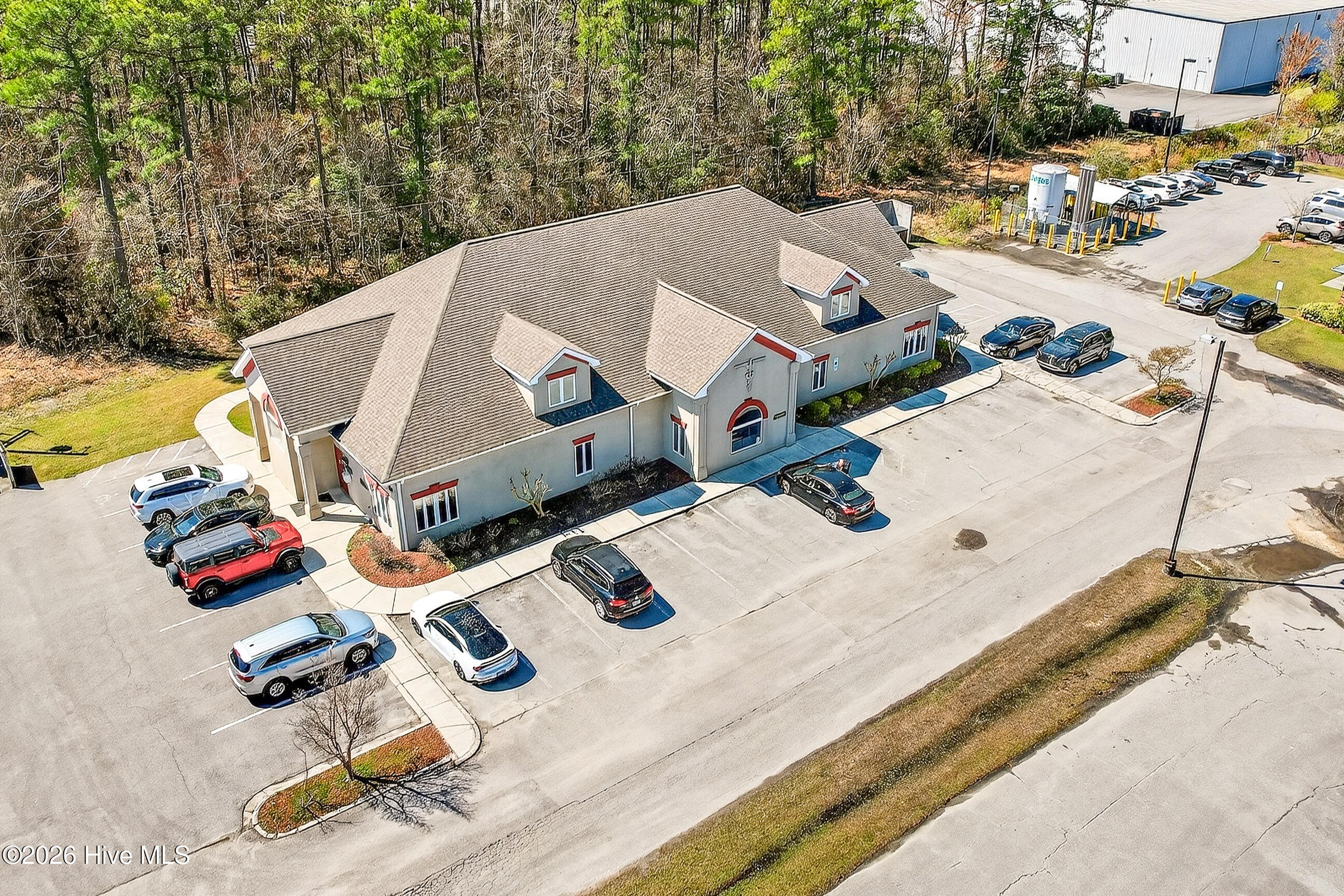 Commercial building with gray walls and red trim, surrounded by a large parking lot and parked cars.