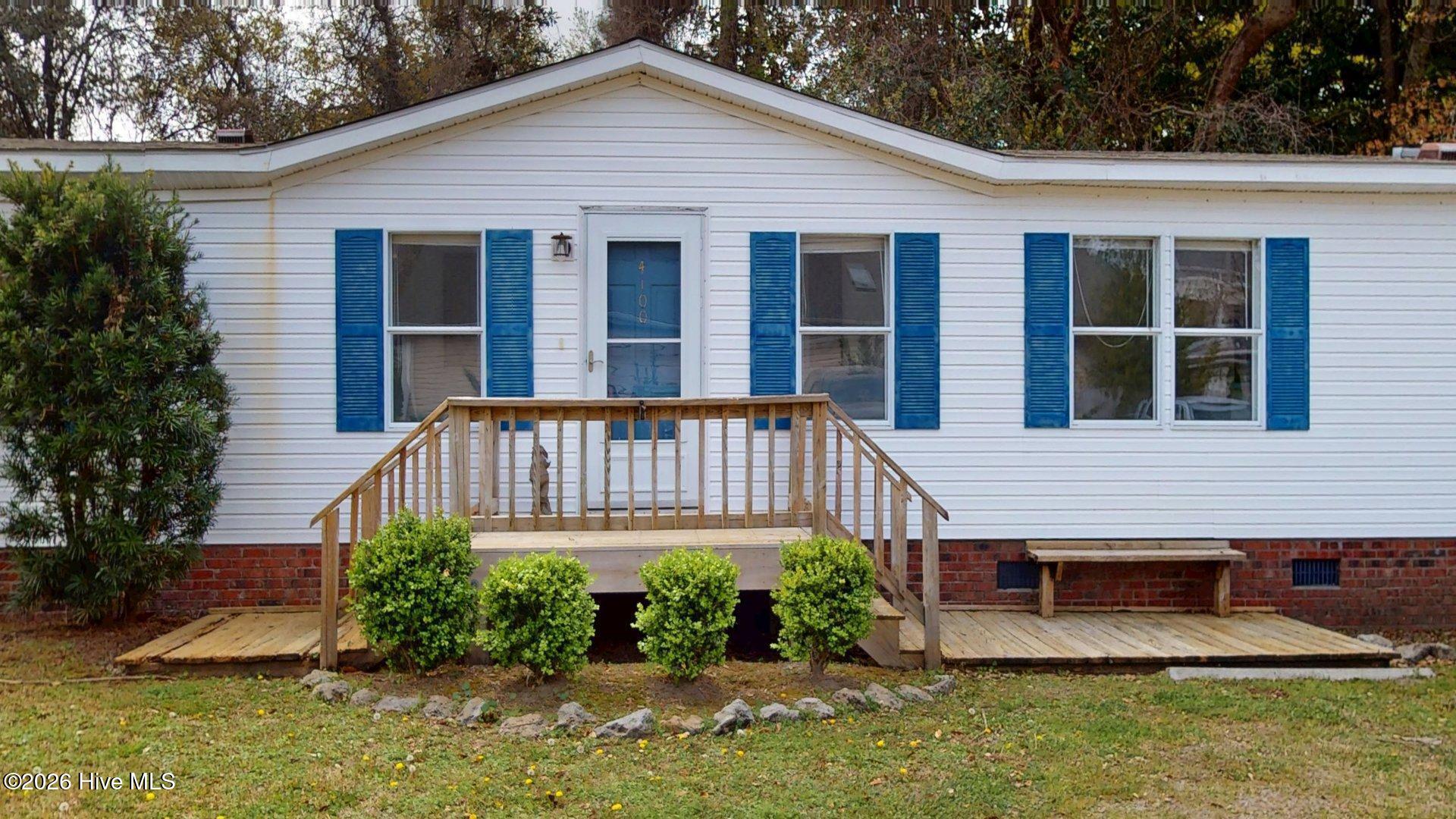 White single-story house with blue shutters, a blue 4100 door, and a raised wooden front porch.