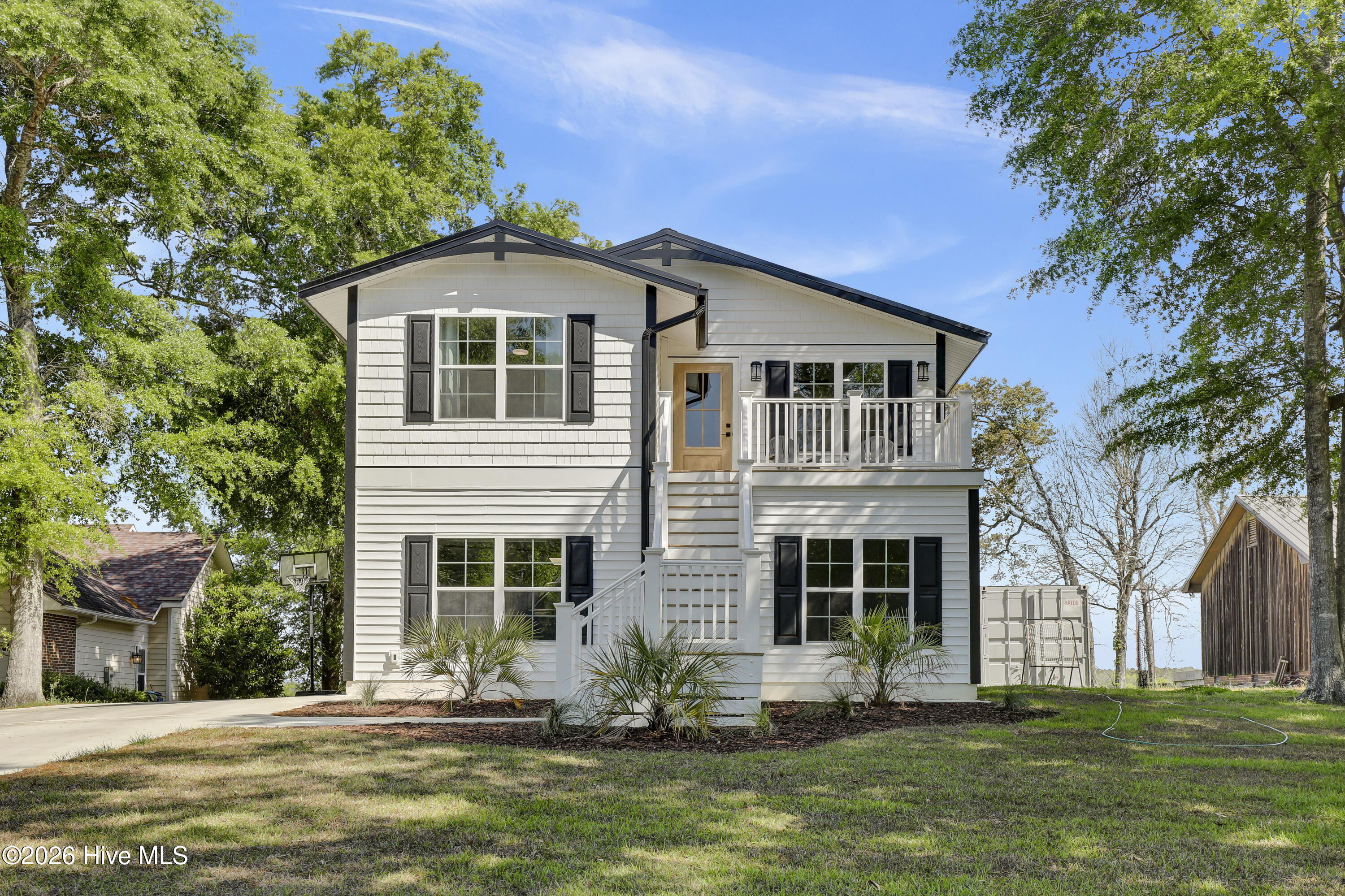 White two-story house with dark shutters, a raised porch, and exterior stairs.