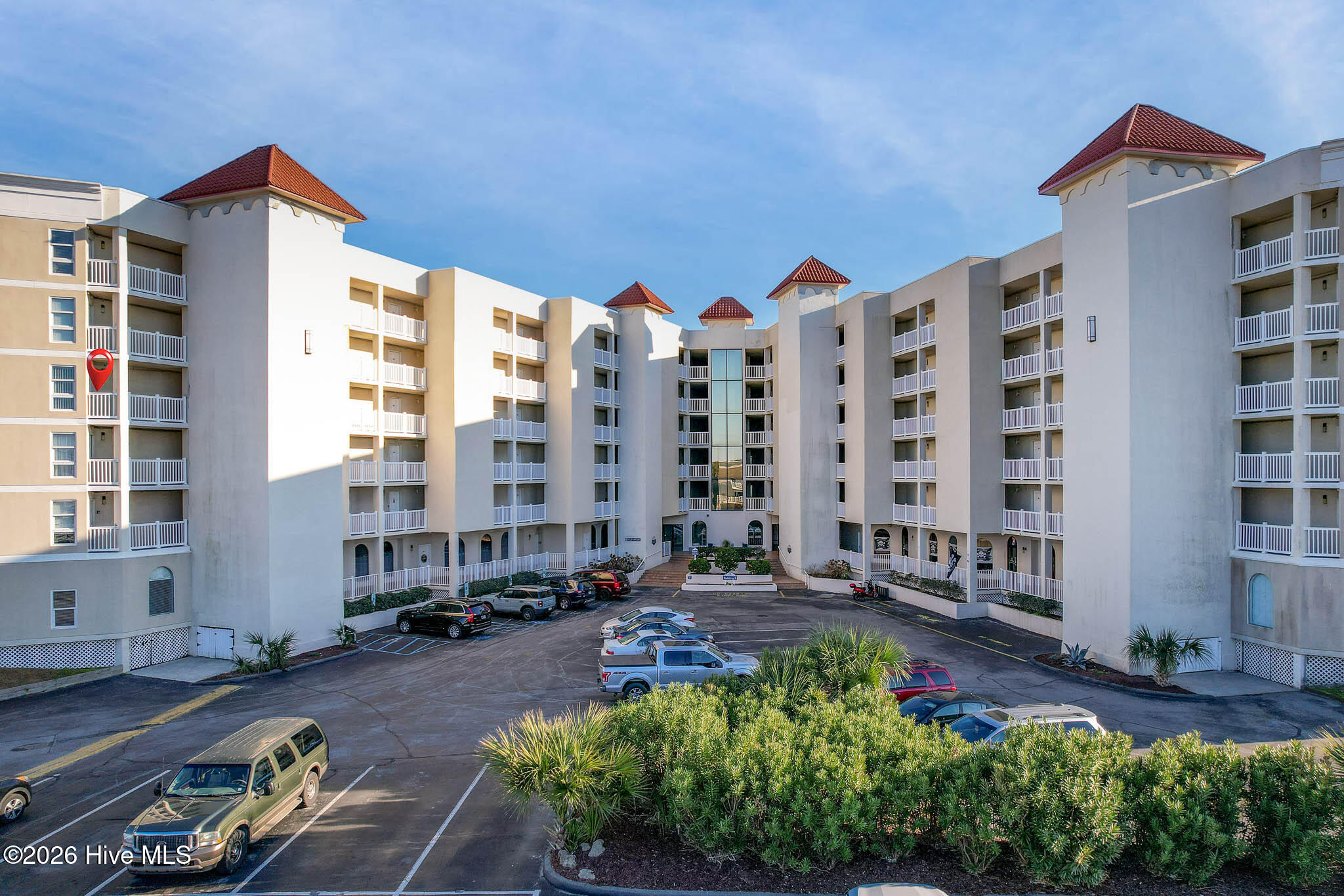 Multi-story condominium with white balconies and red tiled roofs around a central parking area.