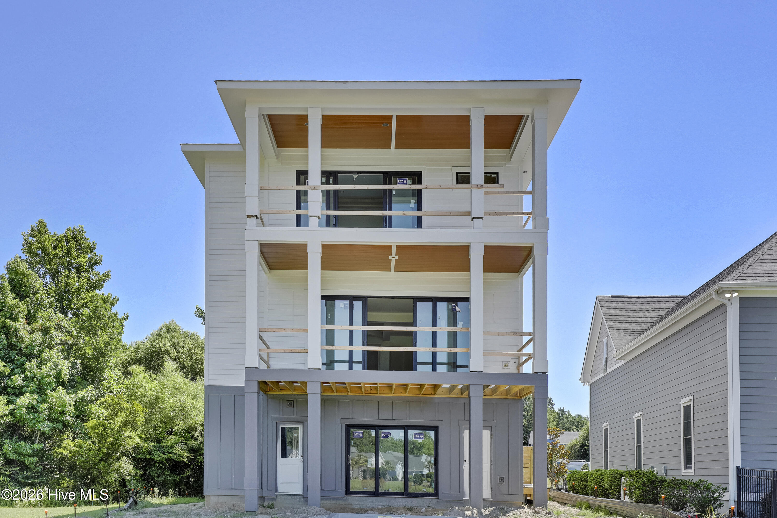 Modern three-story house under construction with stacked balconies and white and gray siding.