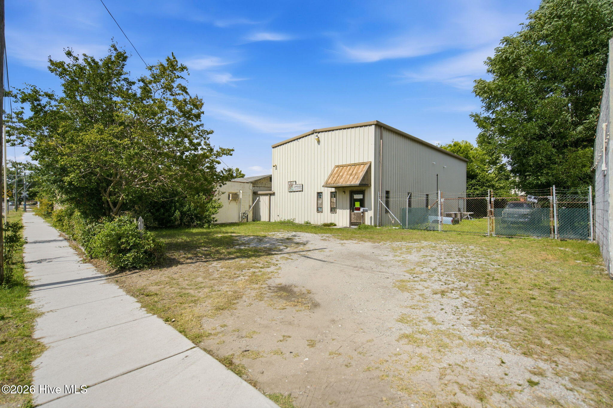 Metal commercial building with a small entrance awning, fenced lot, and gravel parking area.
