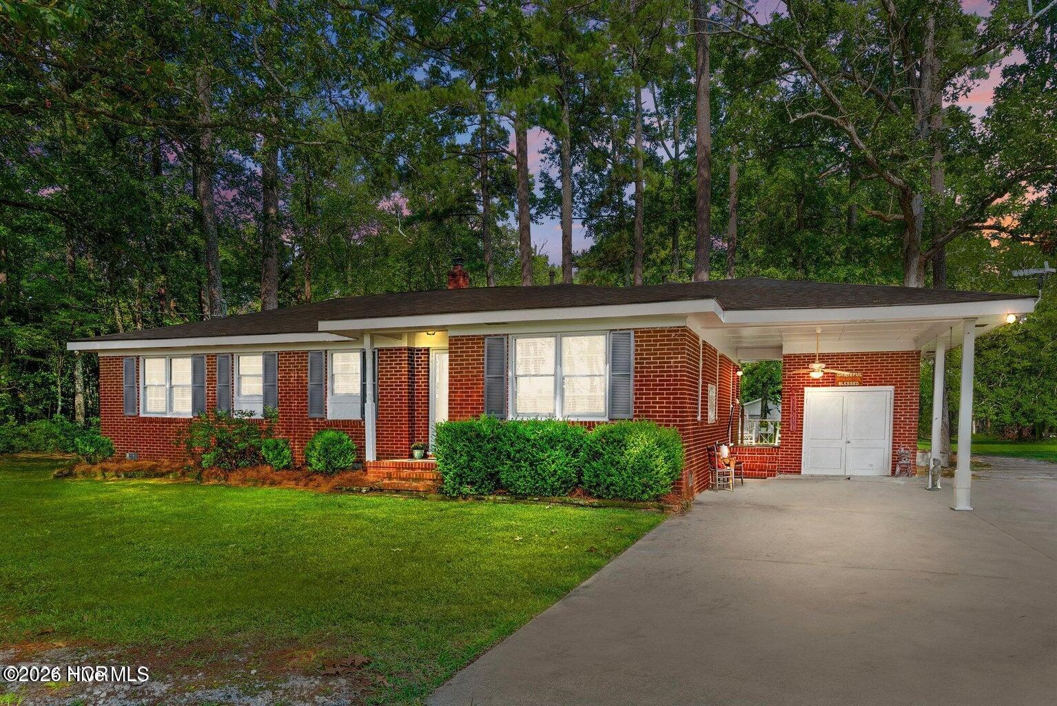 Red brick ranch house with gray shutters, a covered carport, and a broad driveway.