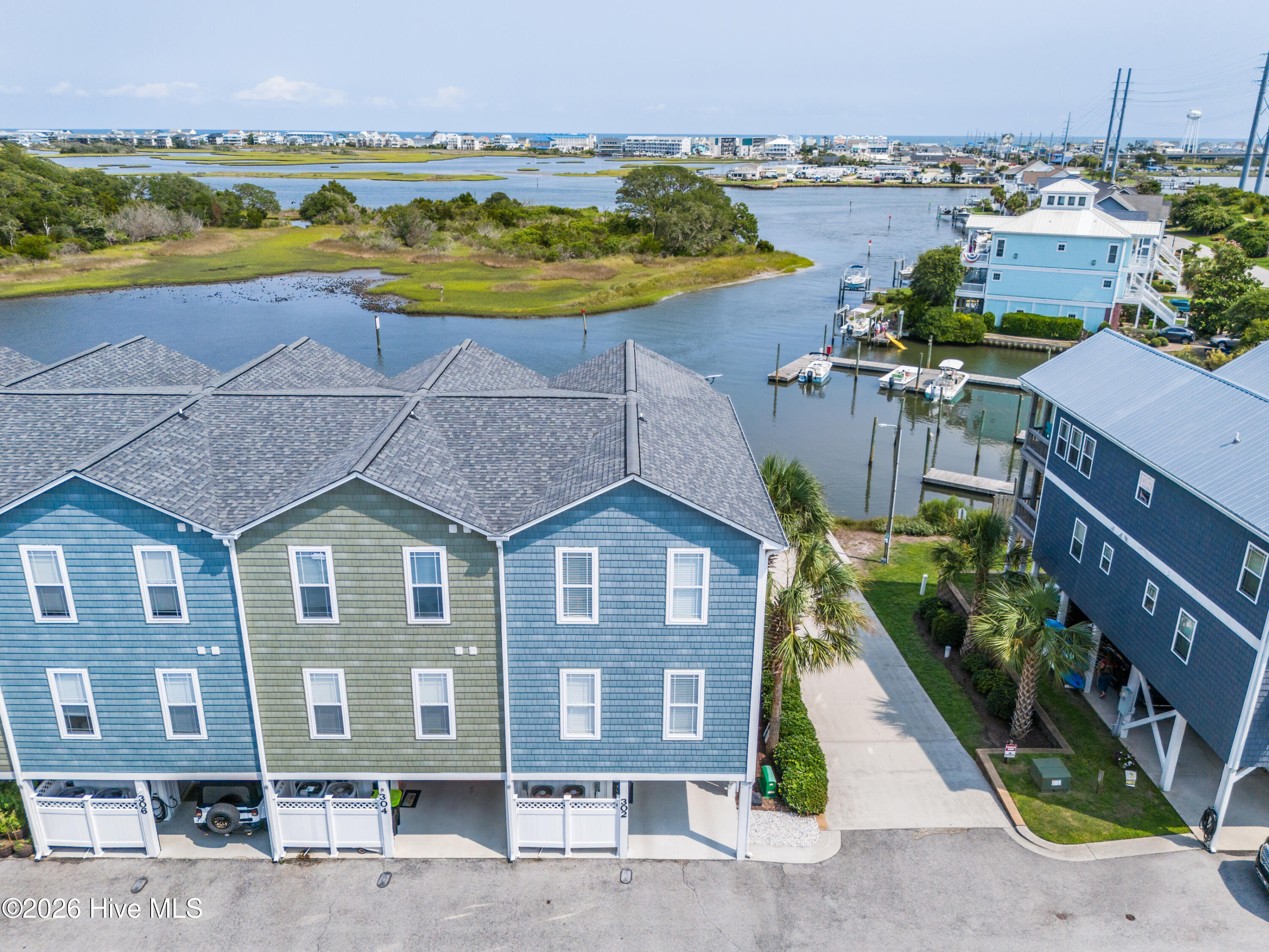 Aerial view of waterfront townhomes beside a tidal channel, with docks, boats, and marsh islands.