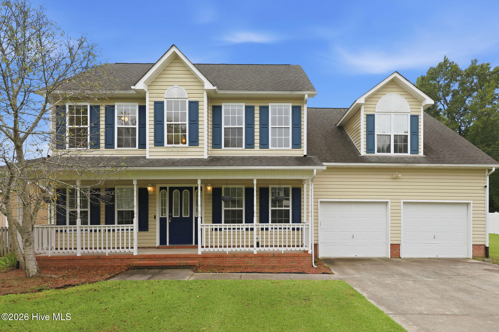 Two-story beige house with blue shutters, a covered porch, and a two-car garage.