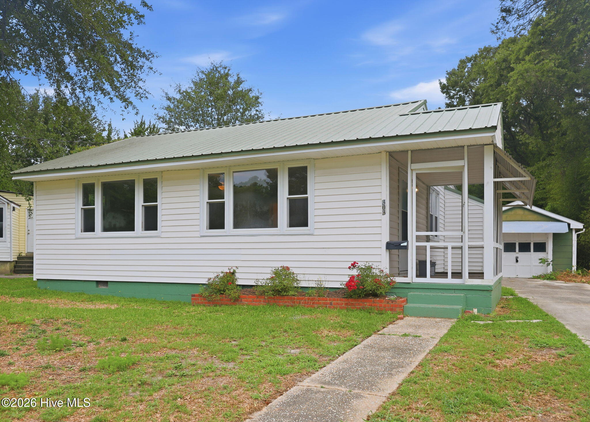 White single-story house with a metal roof, screened porch, and concrete walkway.