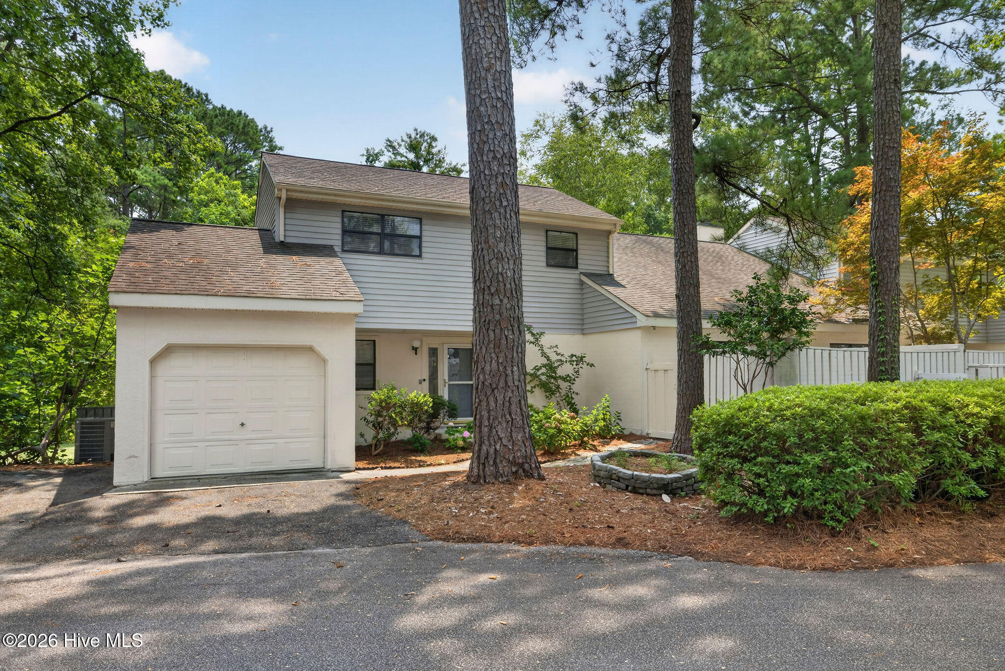 Two-story home with an attached garage, mature pine trees, and a white fence.