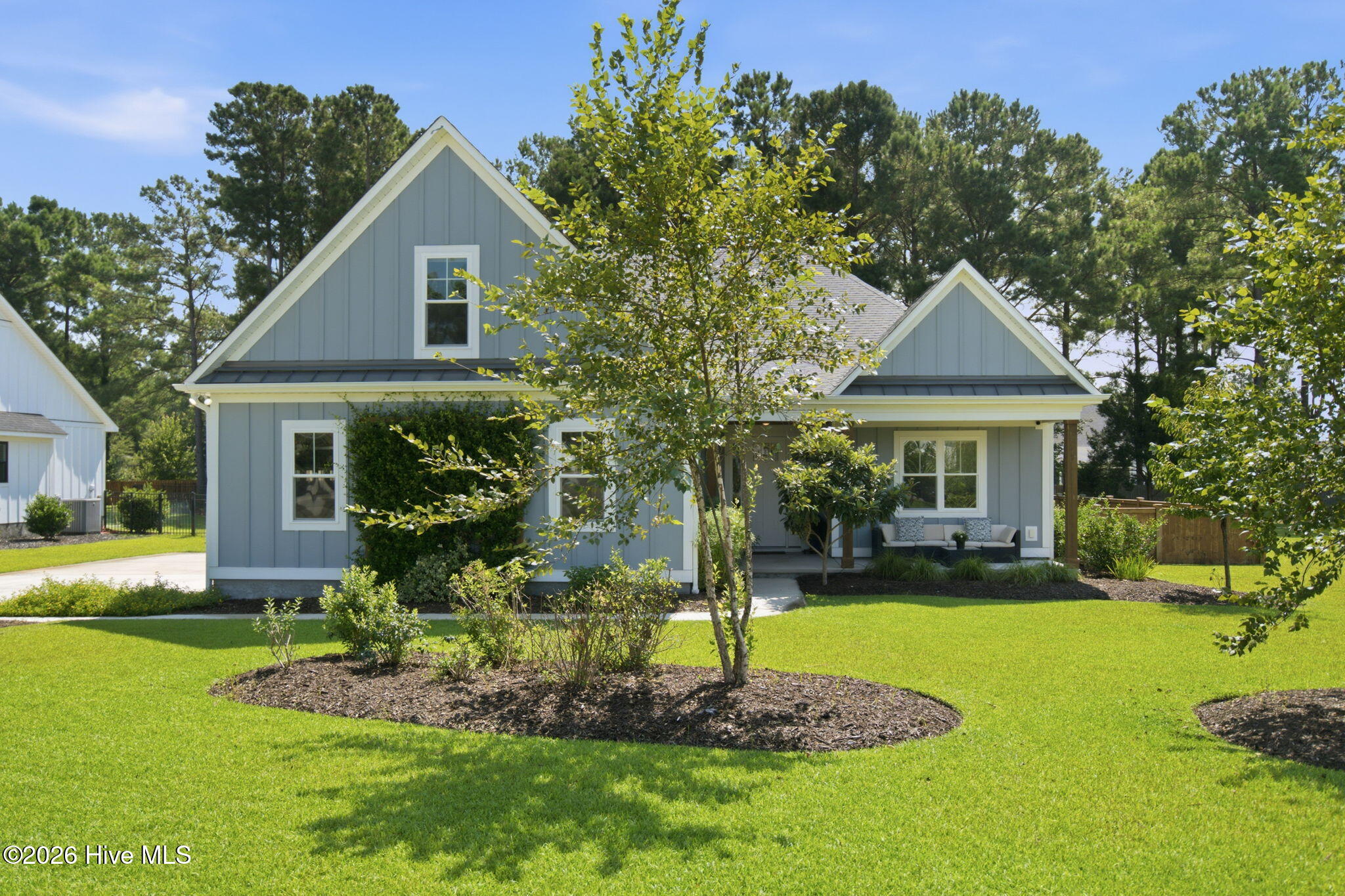 Blue-gray gabled home with a covered porch, landscaped garden beds, and a broad green lawn.