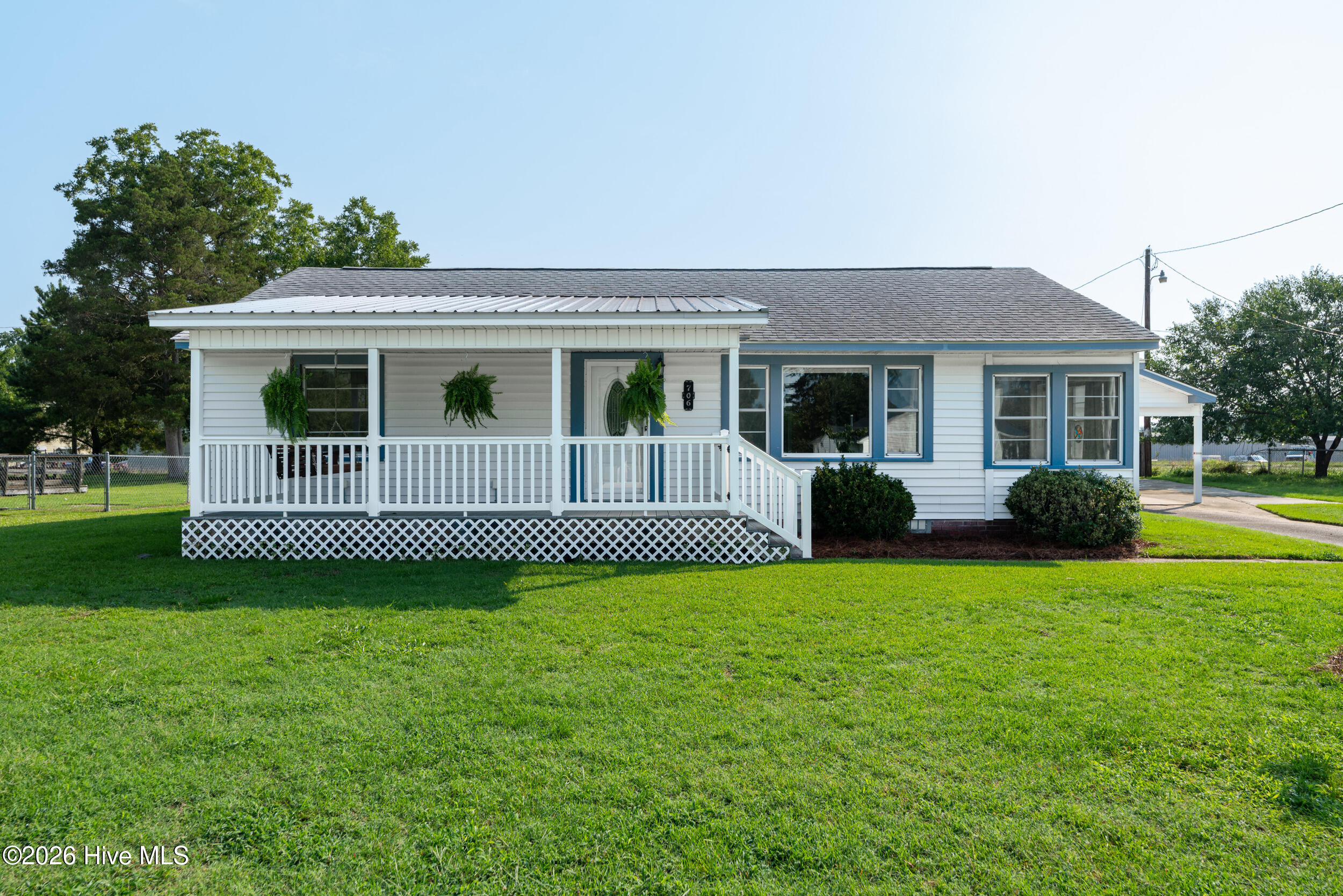 White single-story house with blue-trimmed windows, a covered porch, and hanging ferns.
