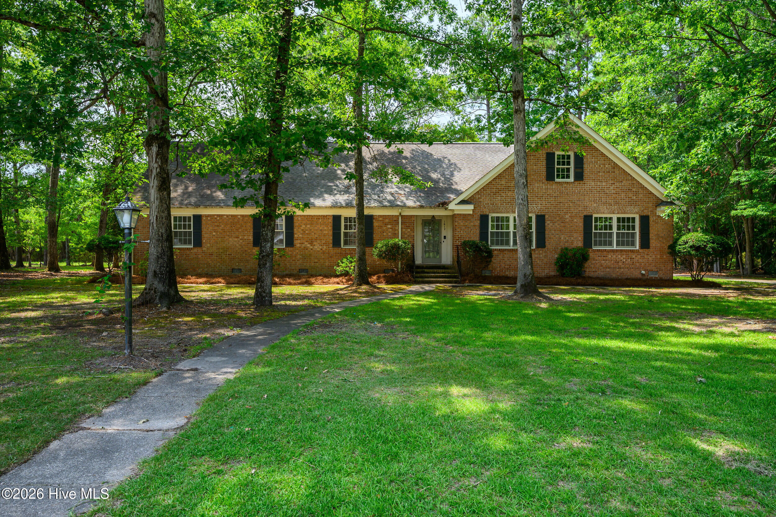 Brick ranch-style home with a front gable, shaded lawn, and curving walkway.