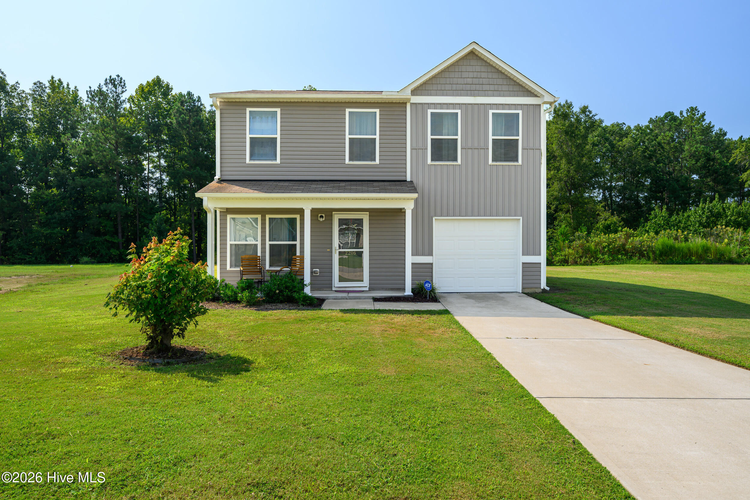 Two-story gray home with a covered porch, attached garage, broad lawn, and concrete driveway.
