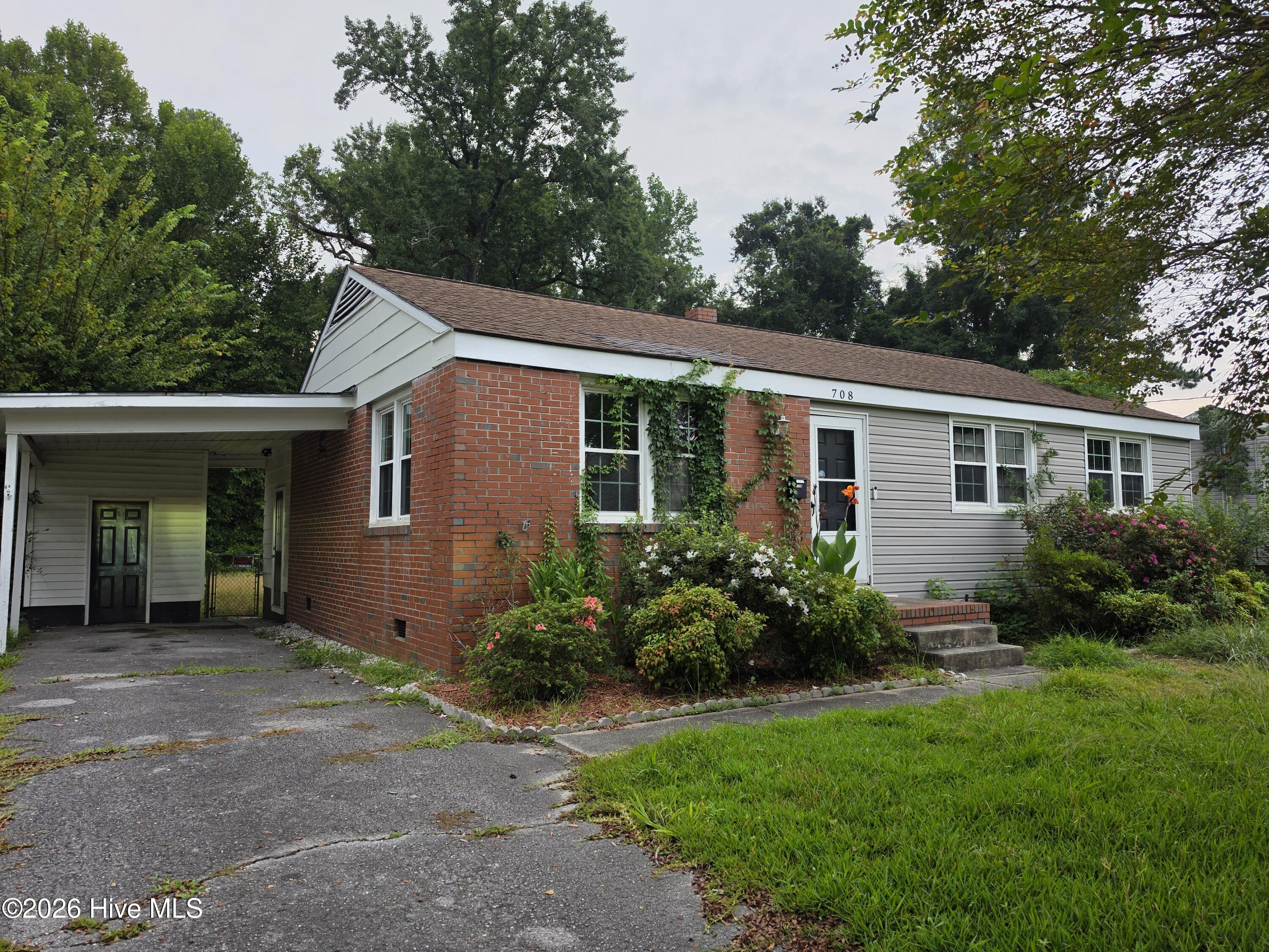 Single-story brick-and-siding home with a covered carport and flowering shrubs.