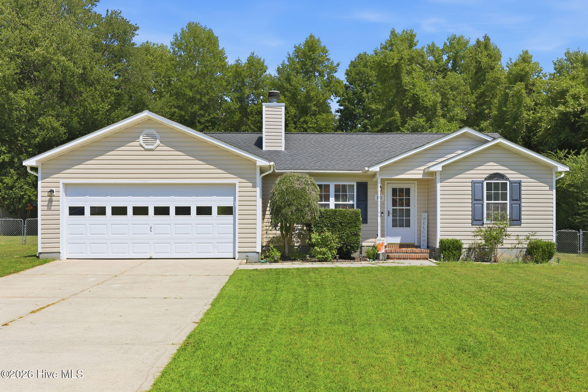 Beige single-story ranch house with a two-car garage, landscaped entry, and broad green lawn.