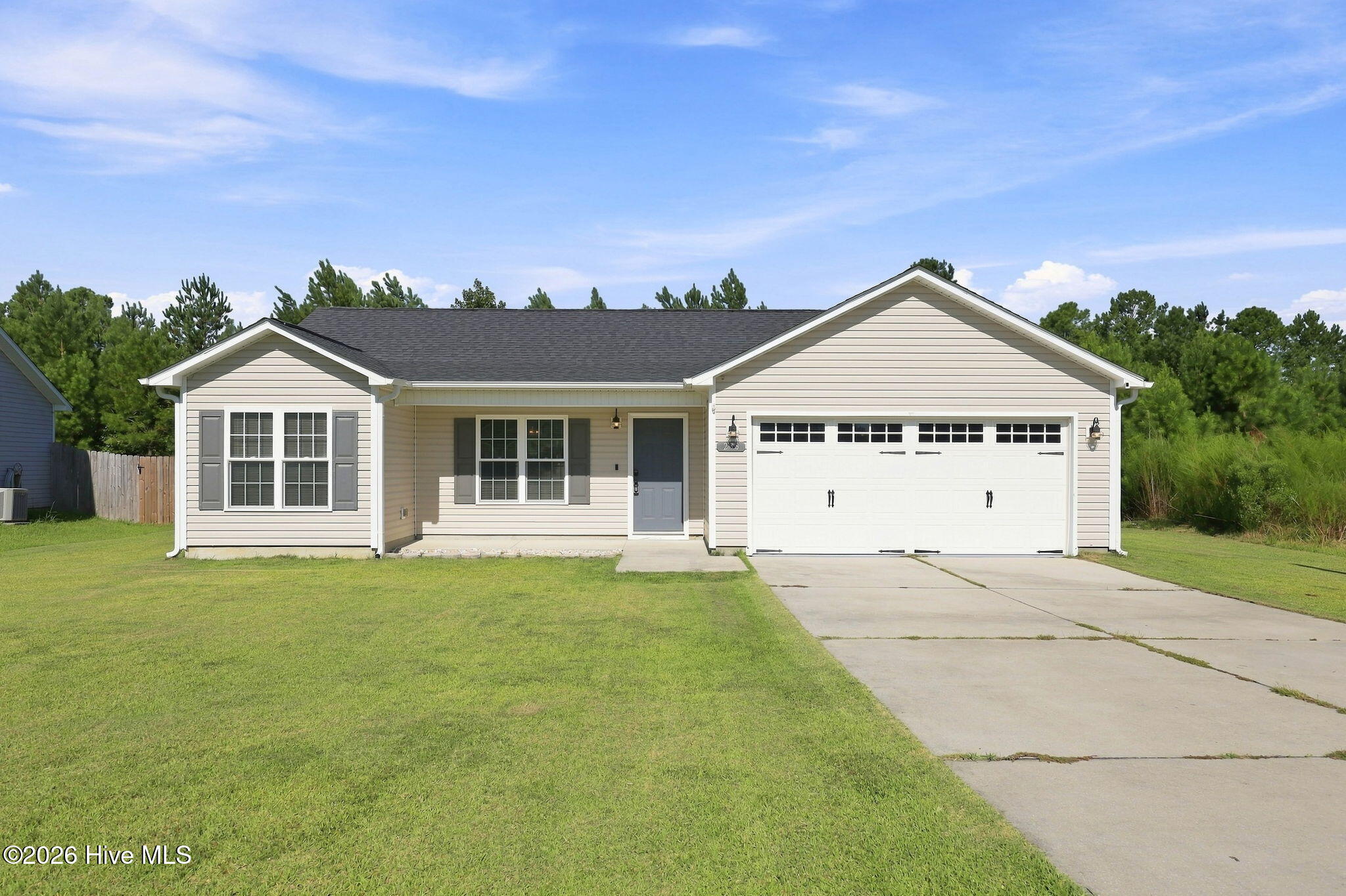 Single-story beige home with a double garage, broad lawn, and concrete driveway.