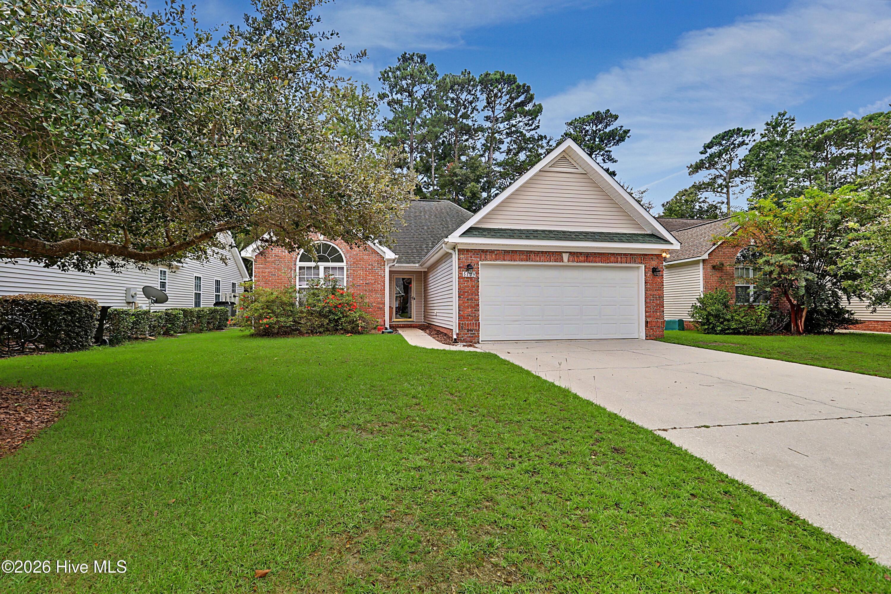Brick-and-siding home with a two-car garage, broad driveway, and mature trees across the front lawn.