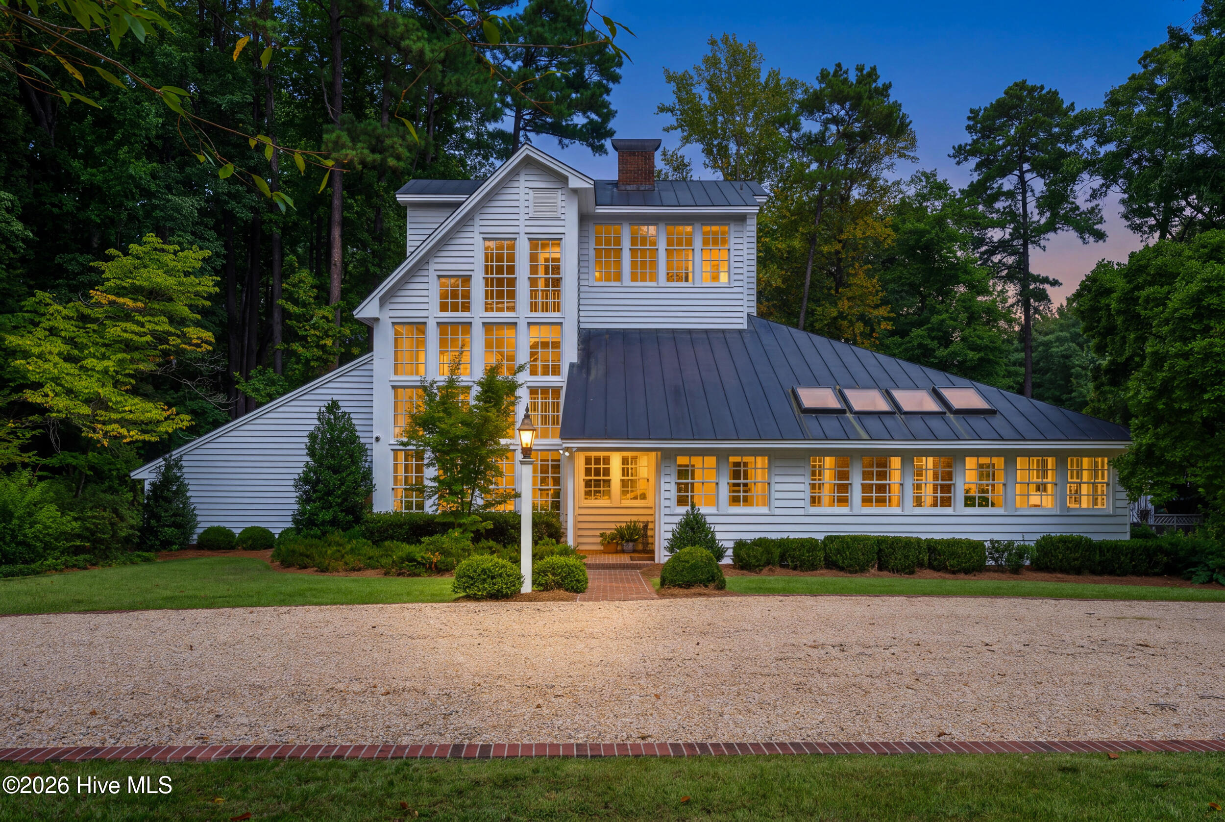 White multi-story home with a metal roof and warmly glowing windows at dusk.