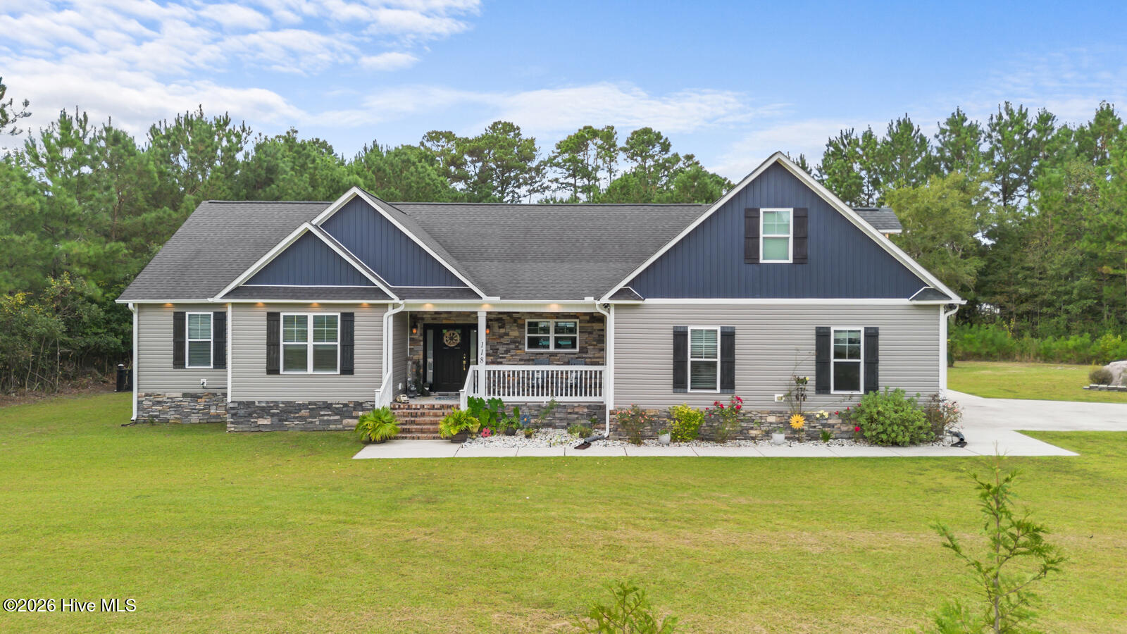 Gray-sided home with dark blue gables, stone accents, a covered porch, and landscaped flower beds.