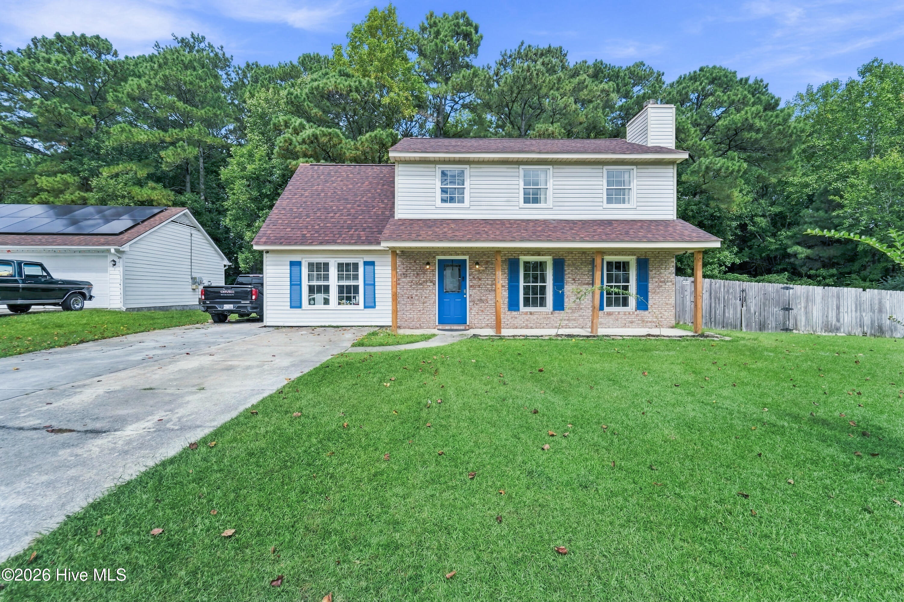 Two-story house with a brick porch, blue door and shutters, and solar panels on the garage.