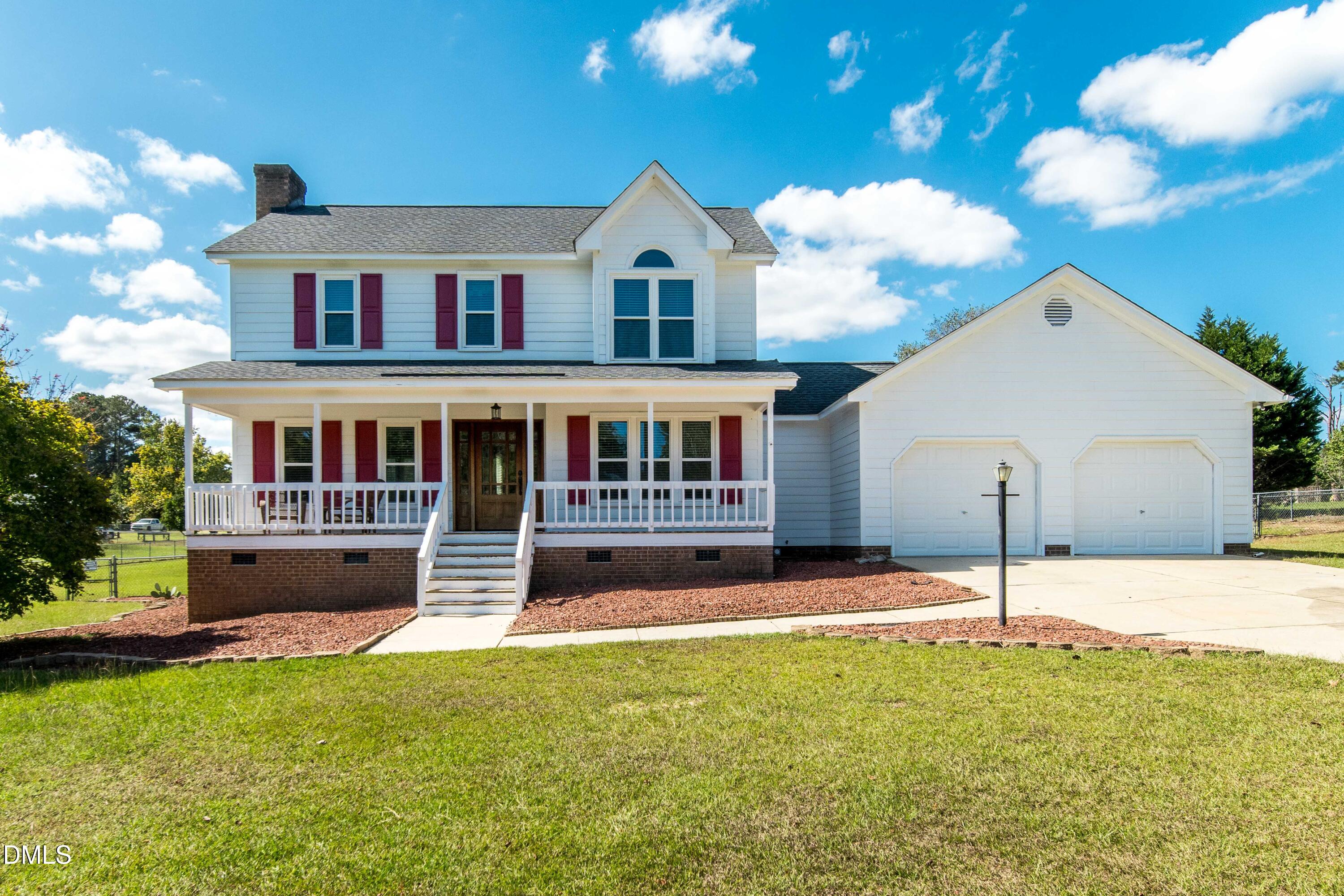 Two-story white house with red shutters, a covered porch, and an attached two-car garage.
