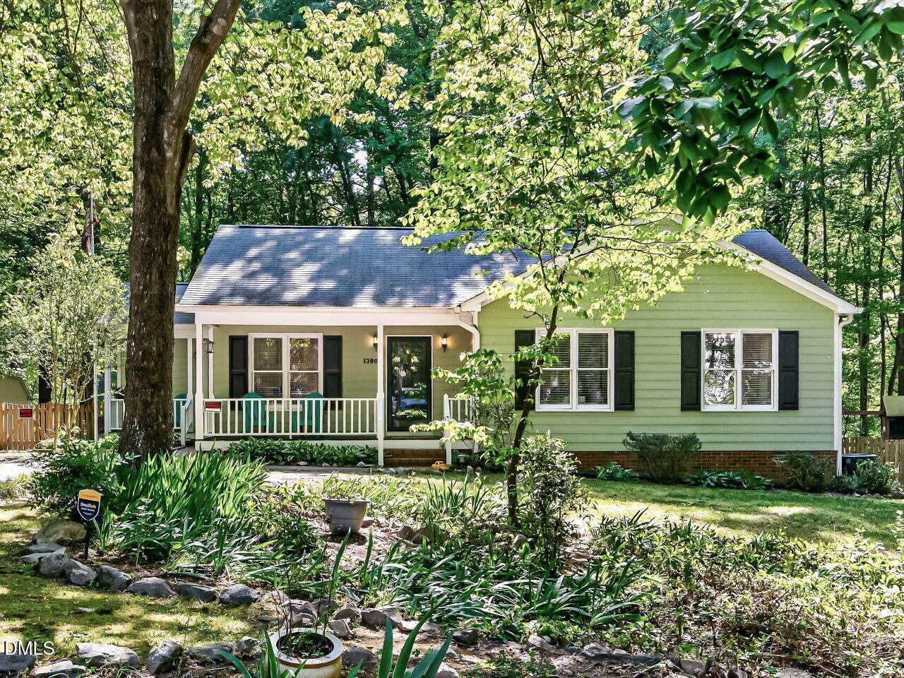 Pale green single-story house with a covered porch, surrounded by mature trees and landscaped gardens.