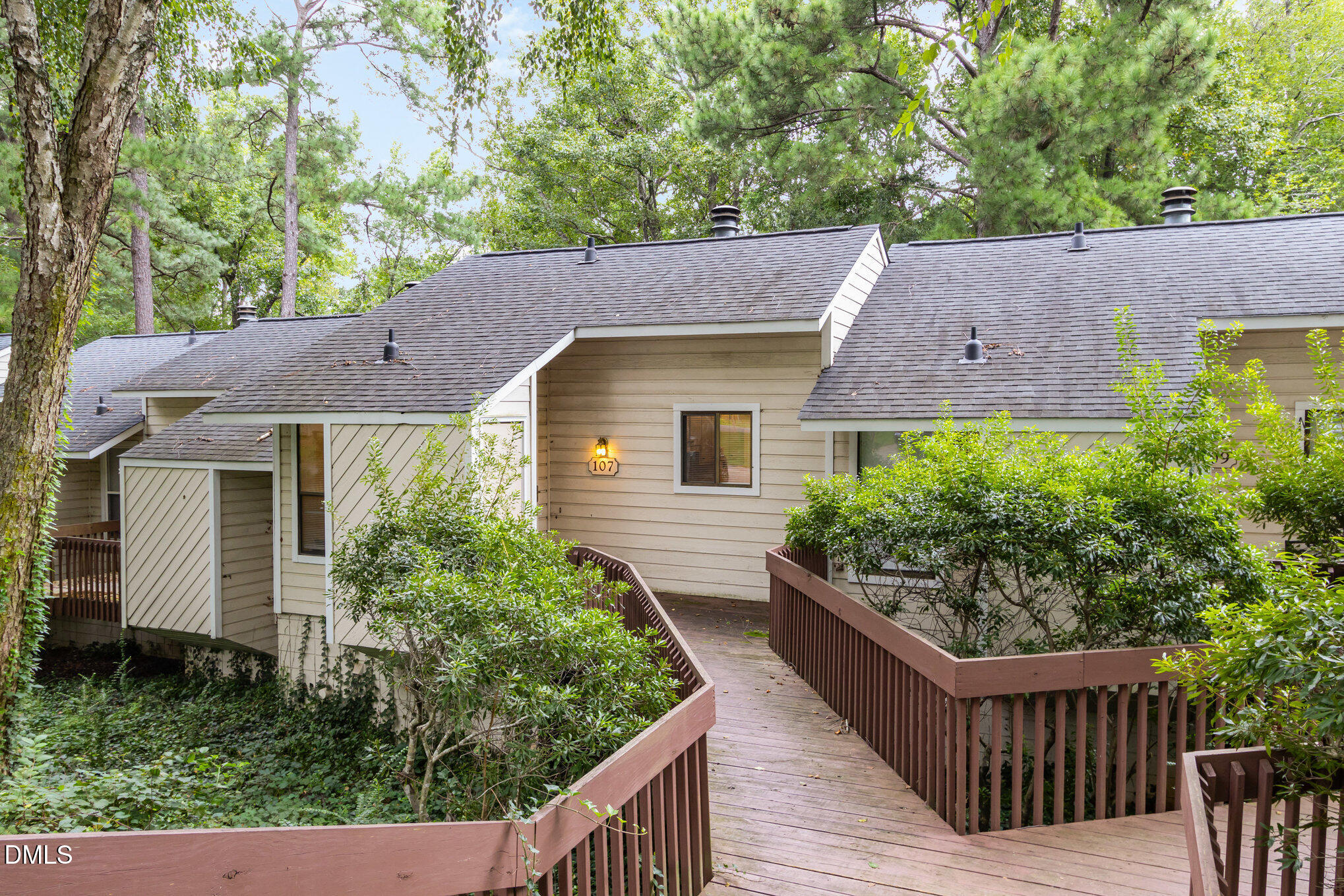 Home at 107 with a raised wooden walkway and mature trees surrounding it.