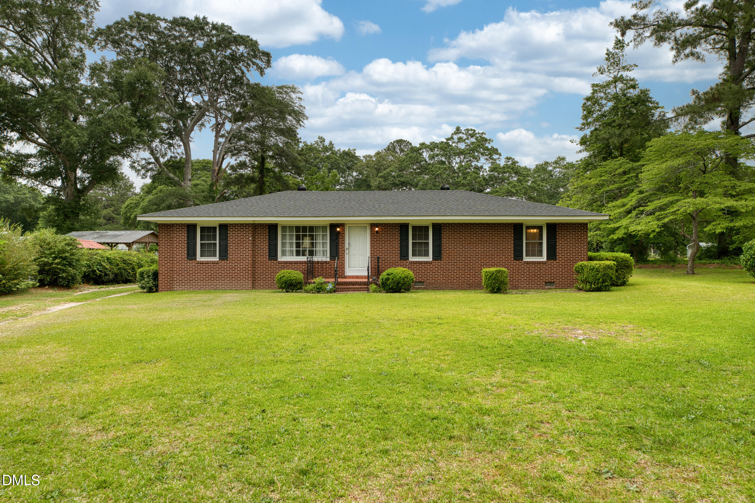Single-story brick ranch house with dark shutters, a wide green lawn, and mature trees.